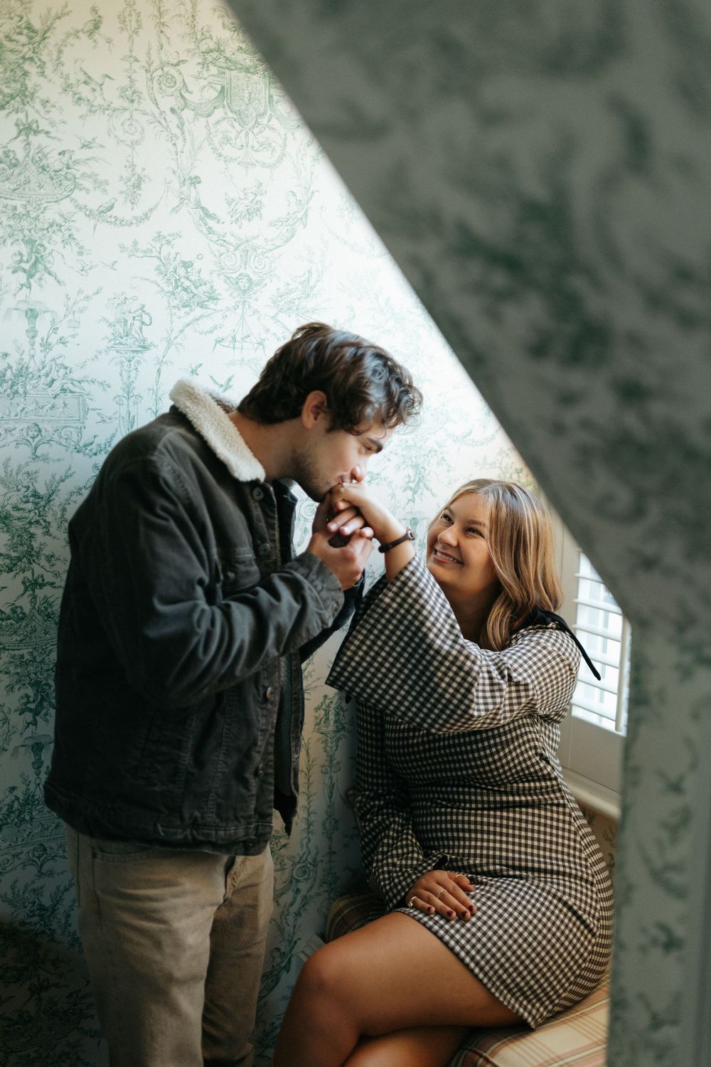 A romantic couple embraces while sitting together against a textured wall in an indoor setting.