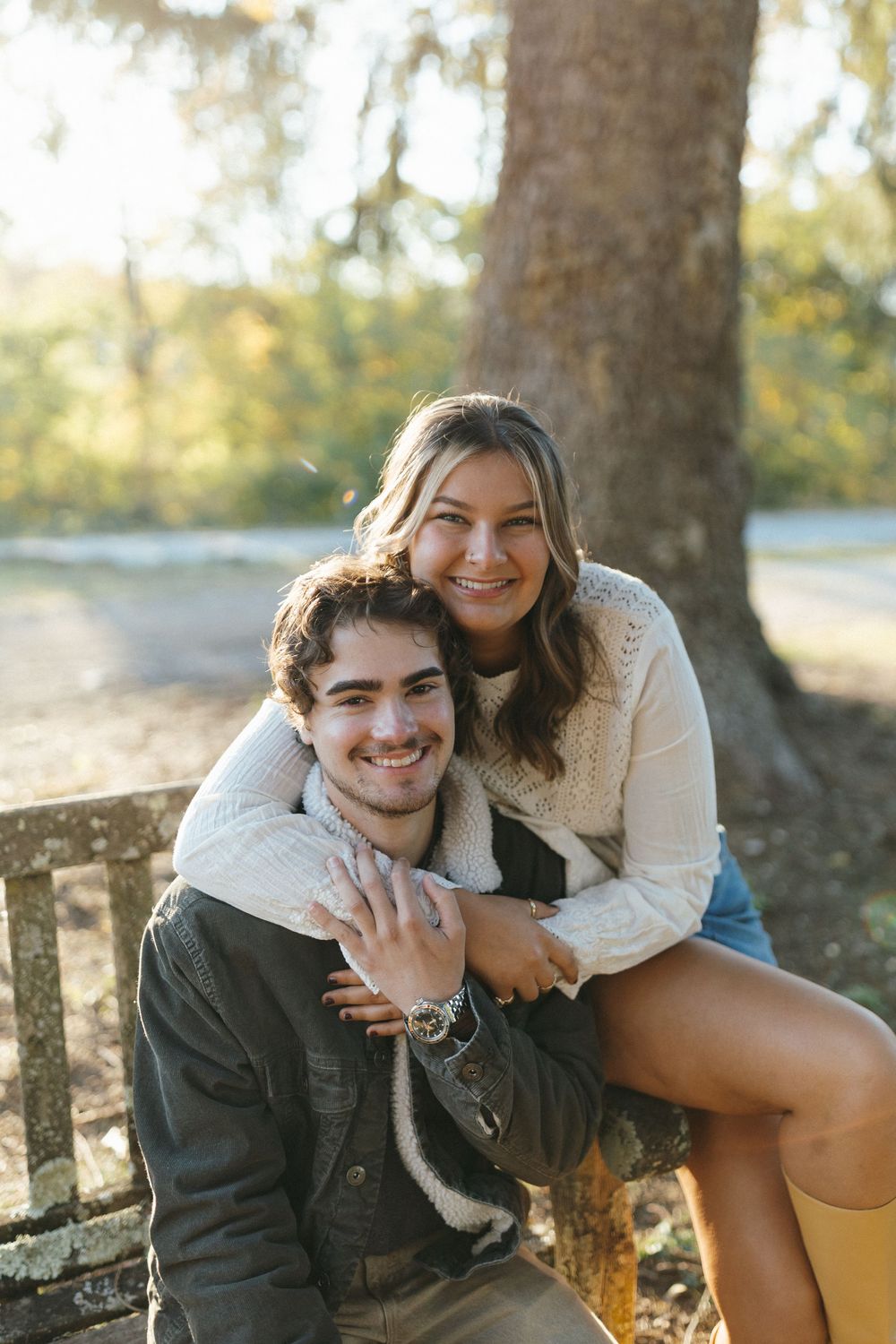 A couple sharing a tender moment while sitting on a wooden bench in a sunlit outdoor setting.