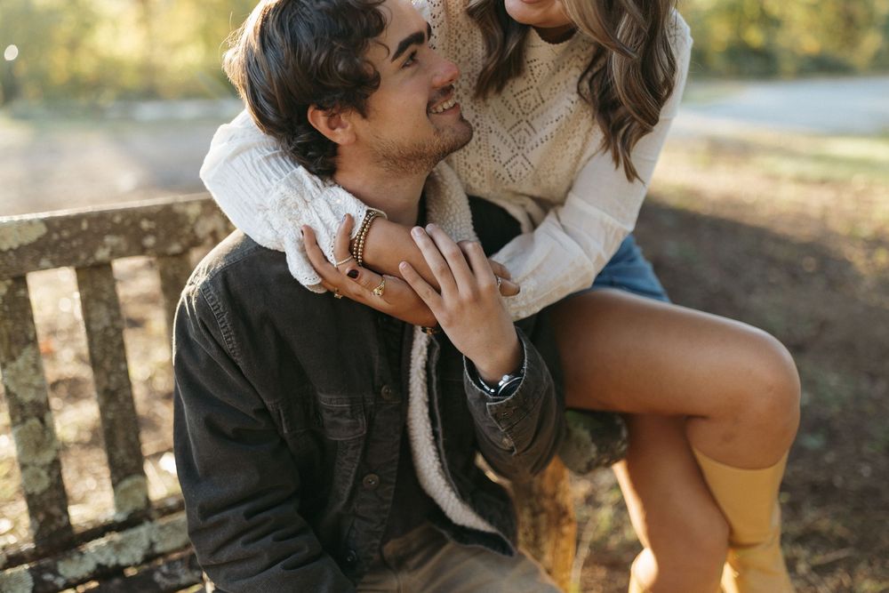 Romantic couple embraces tenderly outdoors during golden hour with sunlight filtering through trees.