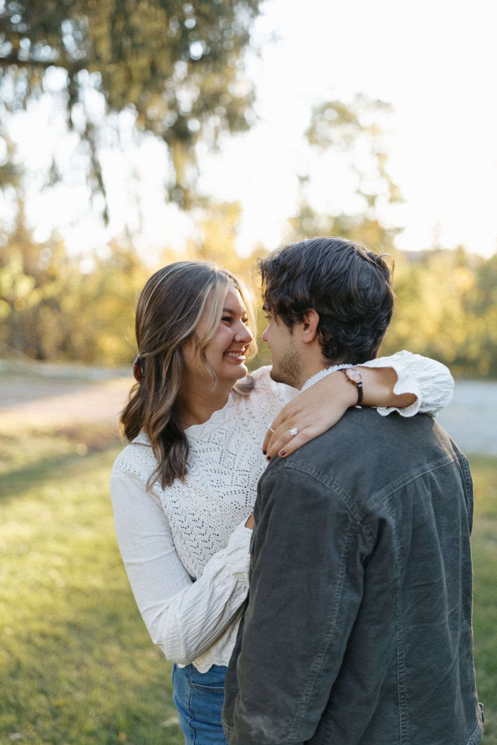 A couple shares intimate moments while standing in a sunny field with trees in the background.