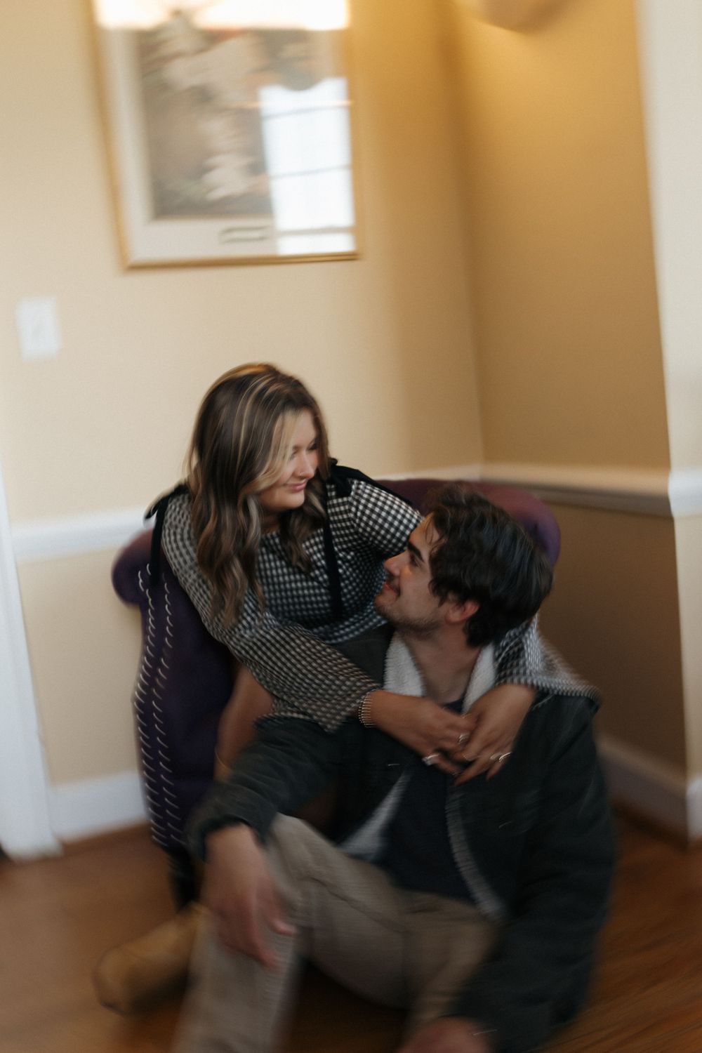 A couple shares an intimate moment on a hardwood floor in a sunlit room.