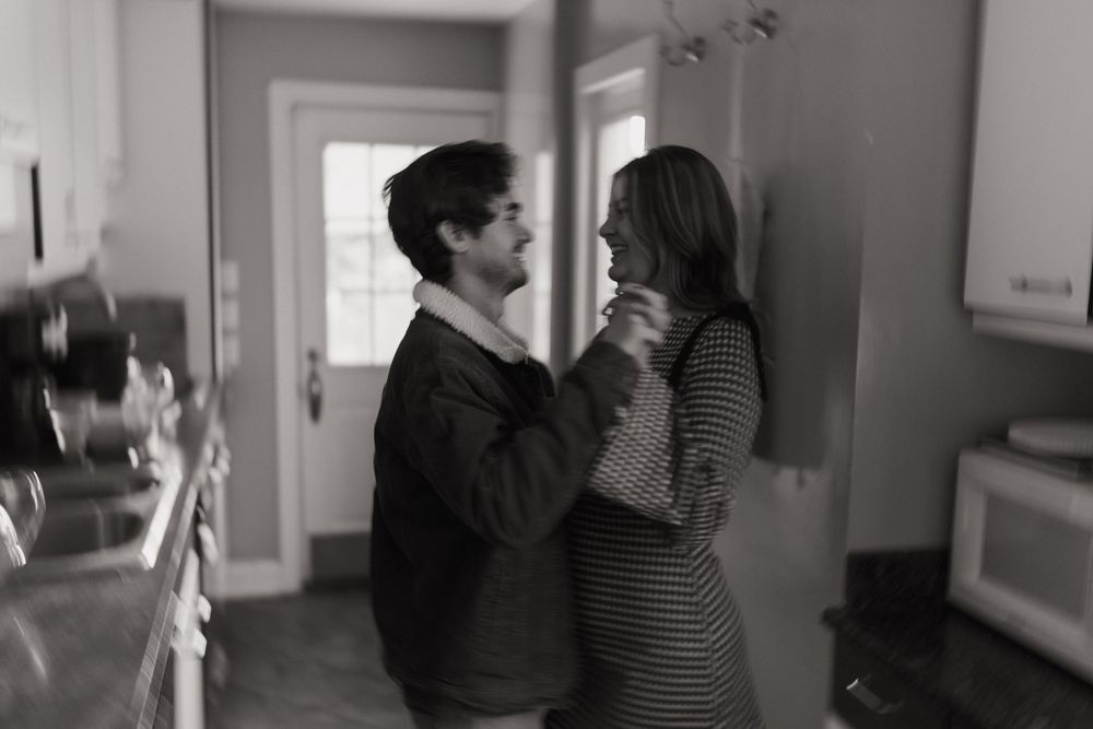 A romantic black and white photo of two people in an intimate moment standing in a doorway.