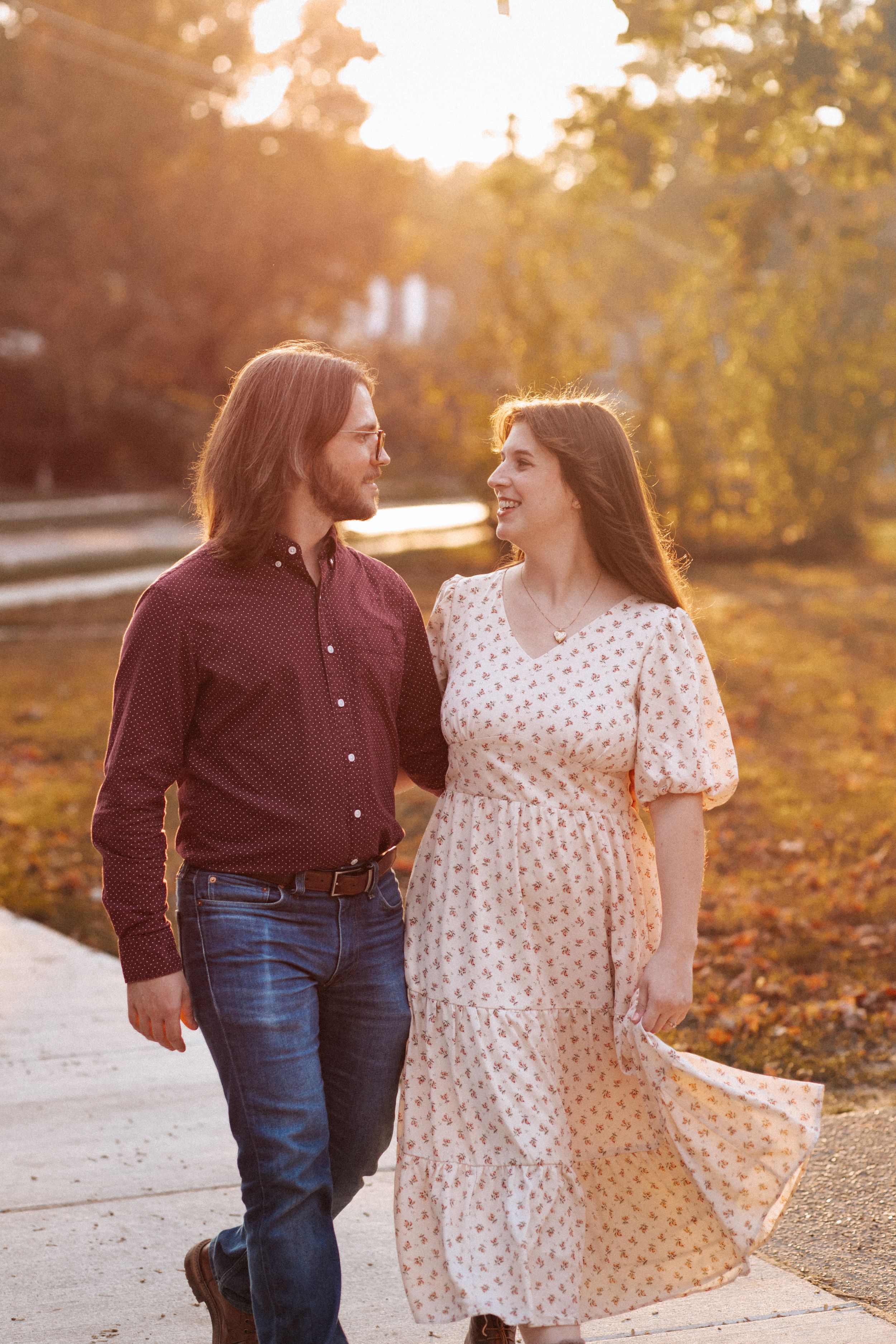 A couple walks together on a path during golden hour sunset, sharing a joyful moment in autumn scenery.