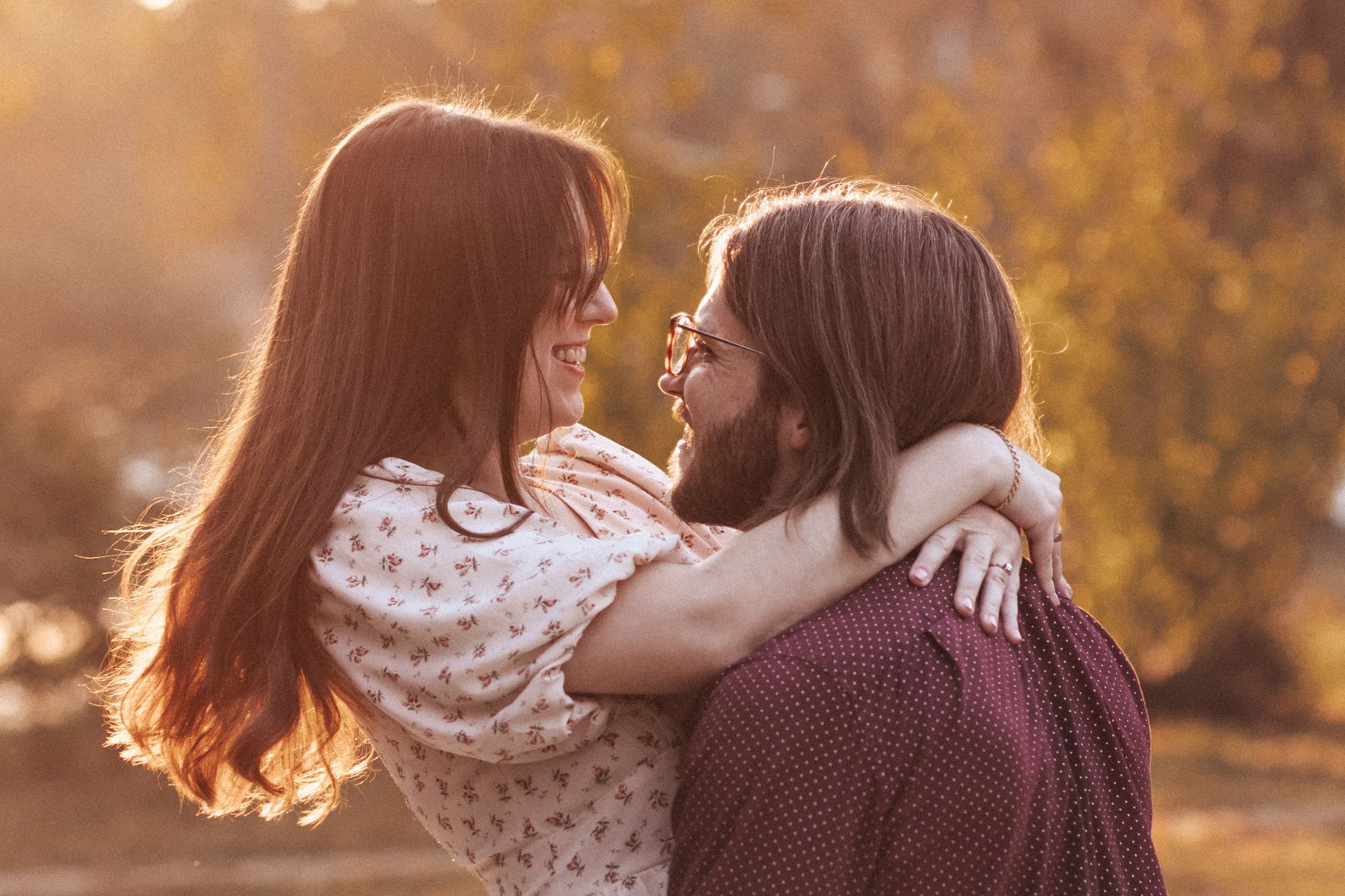 A couple embraces in a golden autumn setting during sunset as fall leaves glow in warm light.