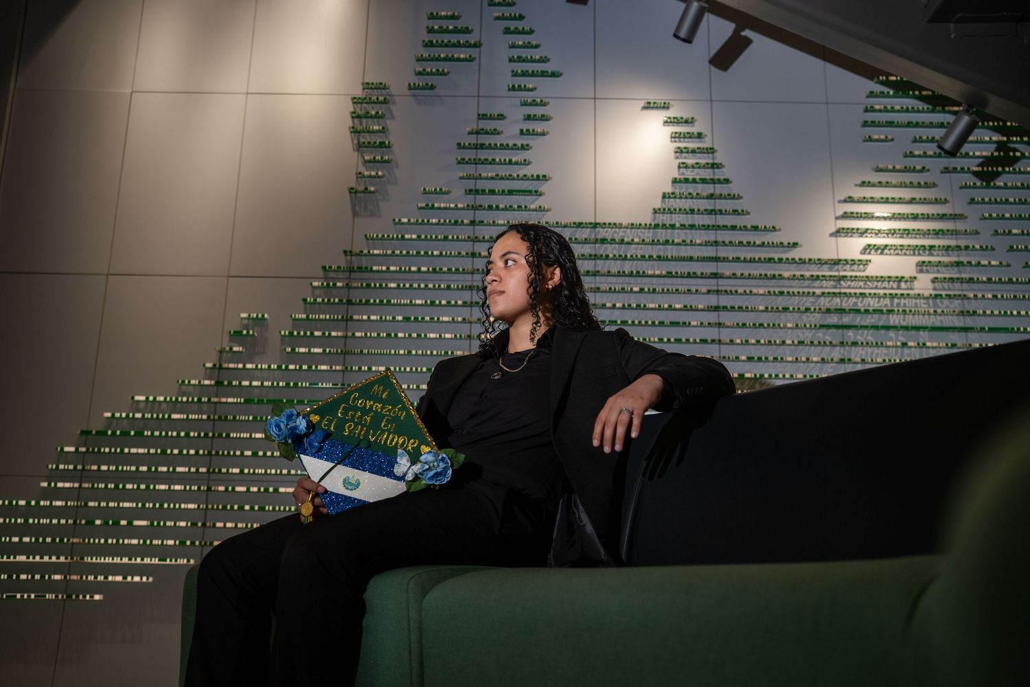 Student sits on dark couch with water bottle against wall with illuminated text display.