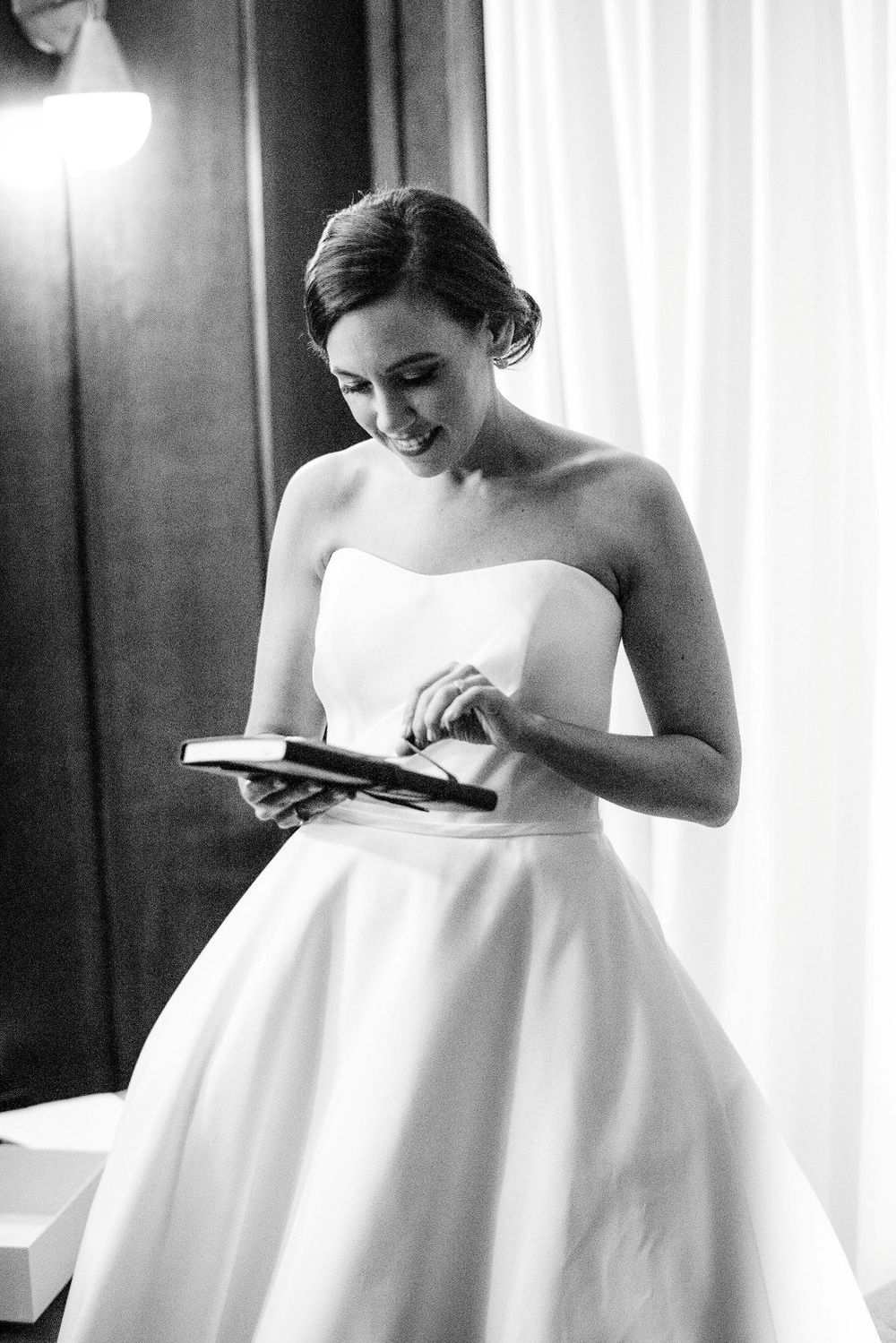 Bride in elegant white wedding dress preparing for her special day in a sunlit room.
