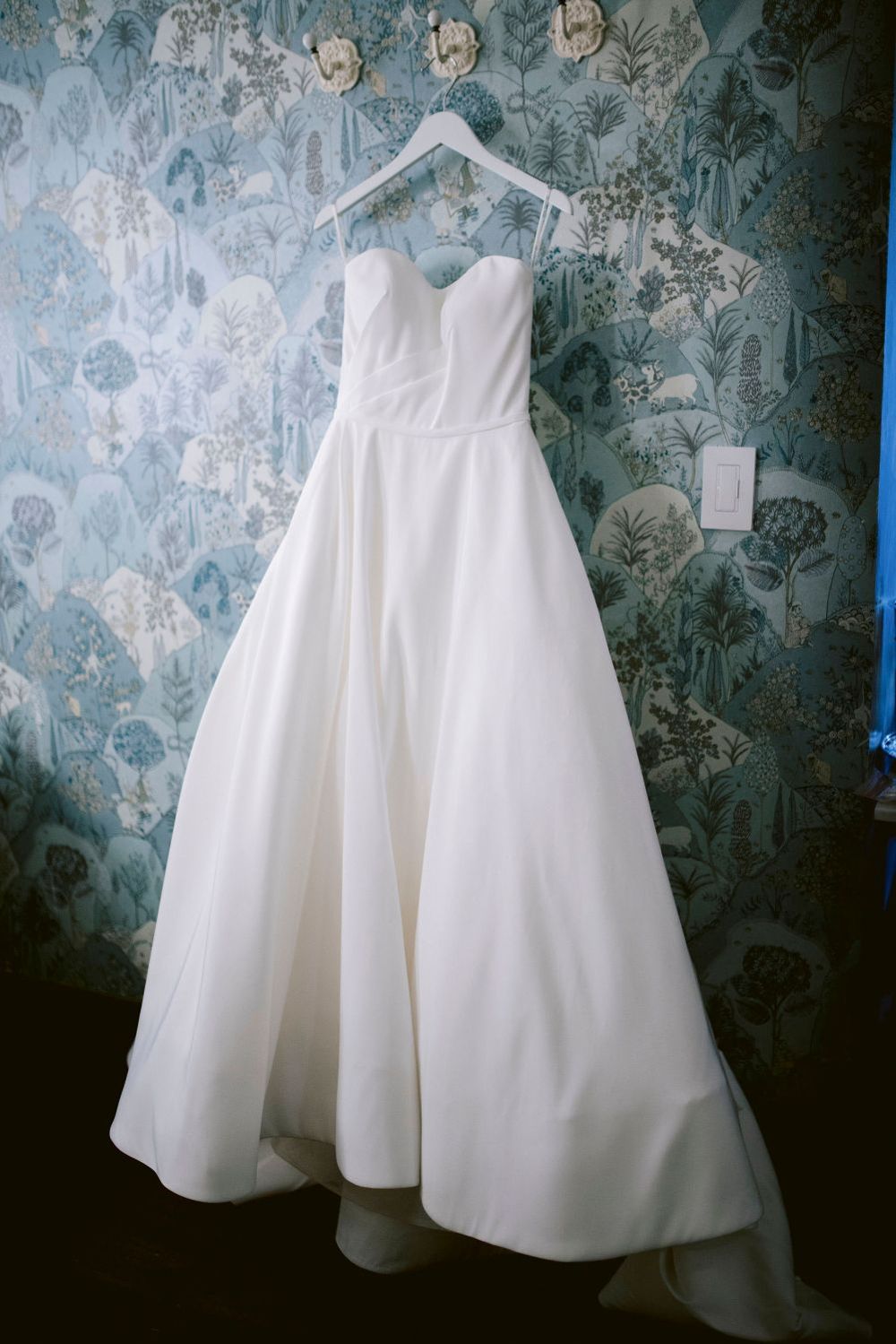 Classic white wedding gown displayed against blue floral wallpaper in a sequence of detail shots.