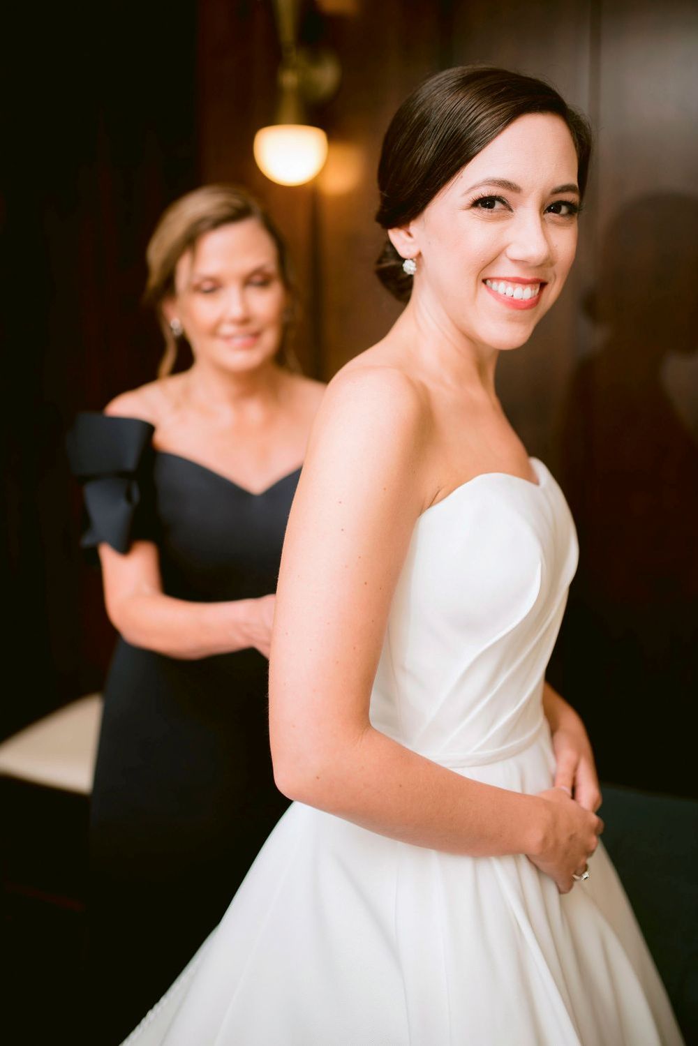 A bride in a classic white strapless gown smiles while getting ready for her wedding day.
