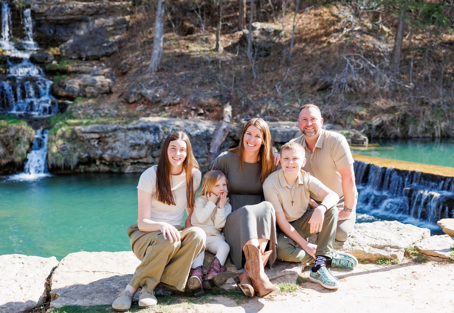 A group of people relax and enjoy the scenery at a scenic waterfall and swimming hole on a sunny day.