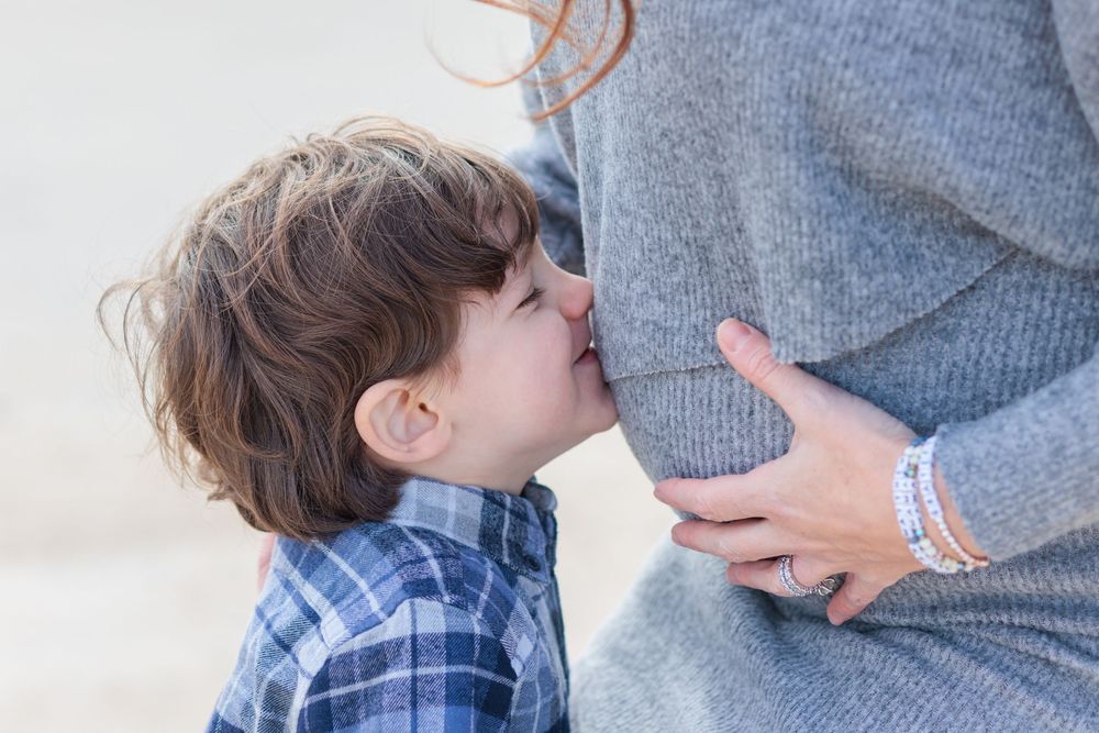 Toddler boy kissing his mom's pregnant belly at Rye Beach.