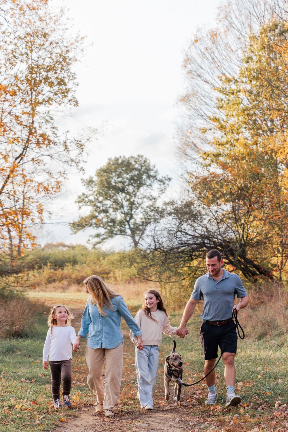 A family walks together through a scenic autumn landscape with golden leaves and trees along a path.