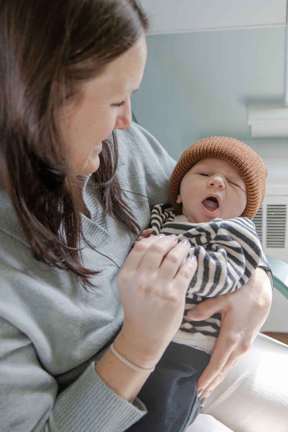 Mom holding her newborn son and looking down at him. Baby is looking at the camera and yawning.