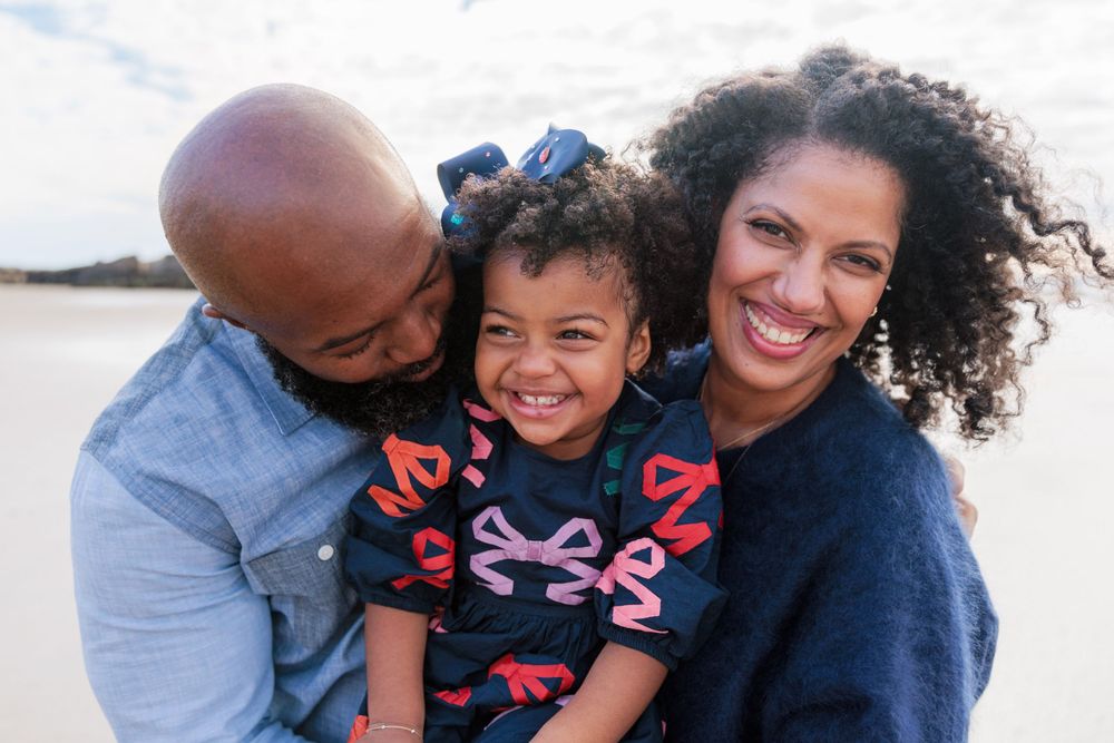 Family of 3 sharing a fun moment of laughter on the beach.