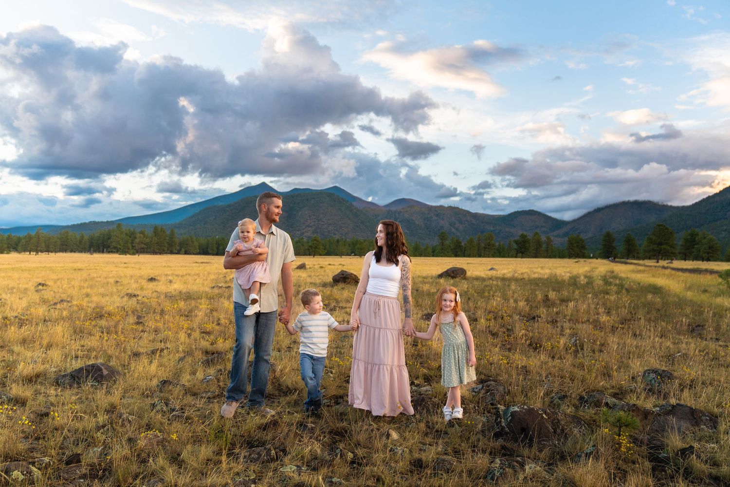 Family standing together in mountain meadow during sunset with dramatic clouds.
