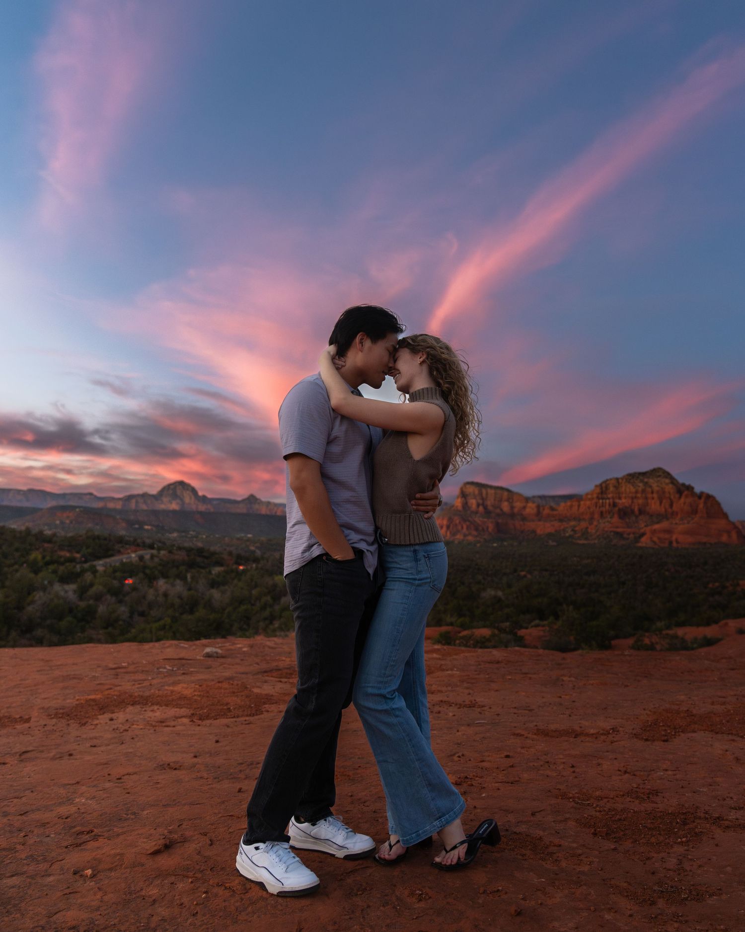 Couple embracing against dramatic desert landscape during pink and purple sunset.