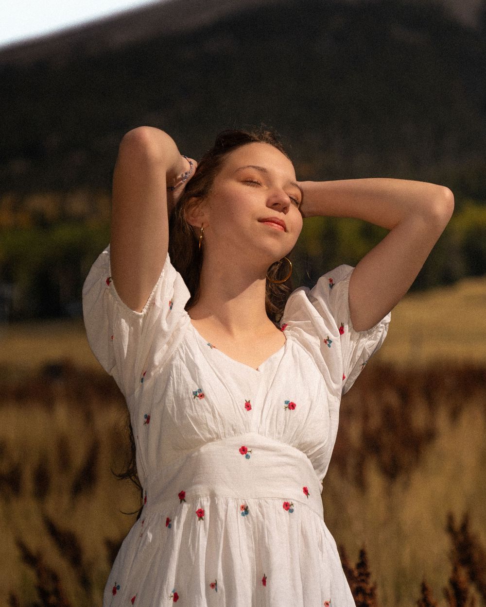 Person in white dress stretches arms overhead in golden sunlit field.