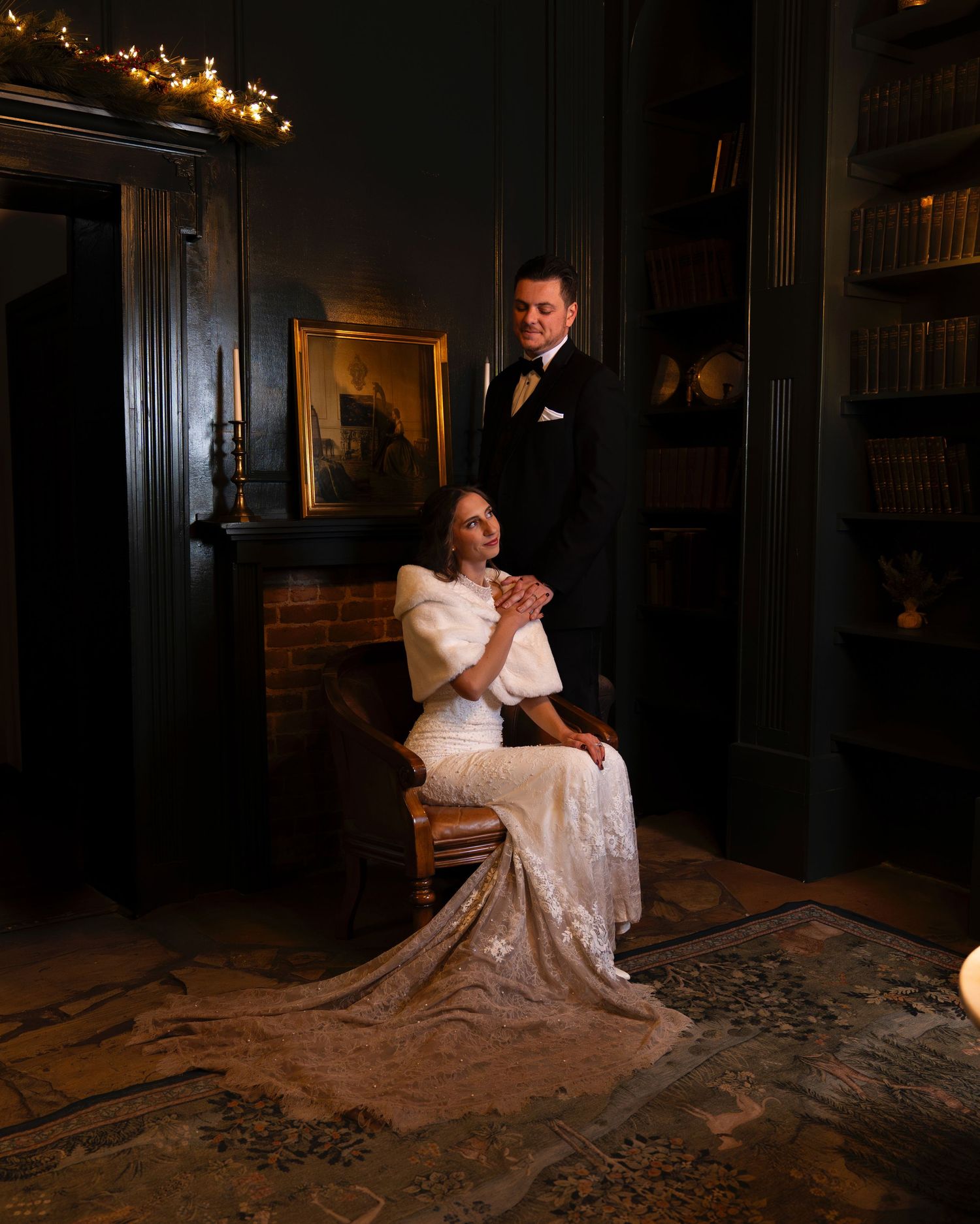 Elegant couple in formal attire posing in dimly lit vintage room with string lights.