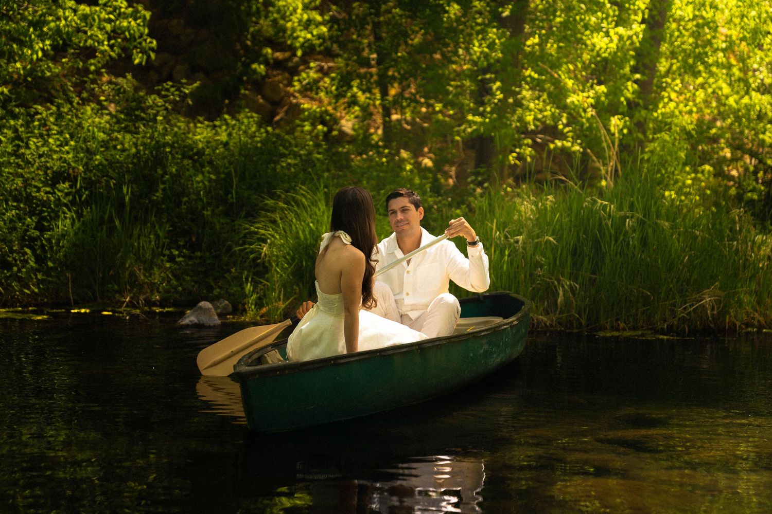 Couple enjoying romantic canoe ride through lush green waters at sunset.