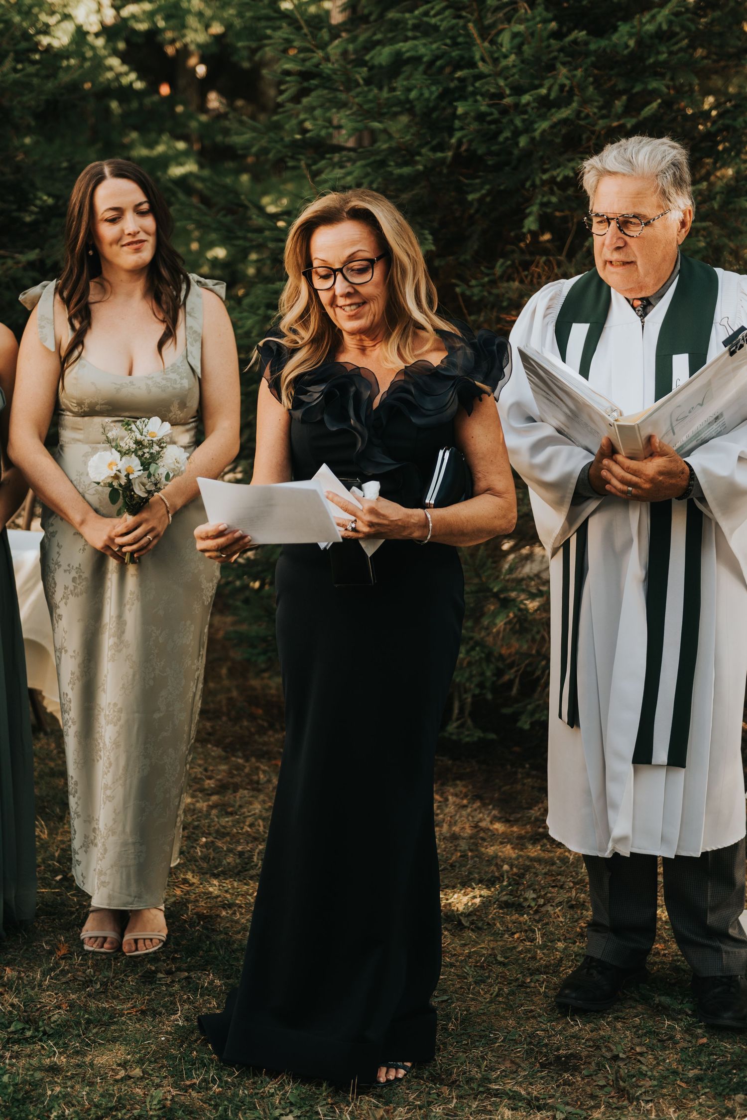 Wedding party members in black and white attire stand together holding bouquets during an outdoor ceremony.