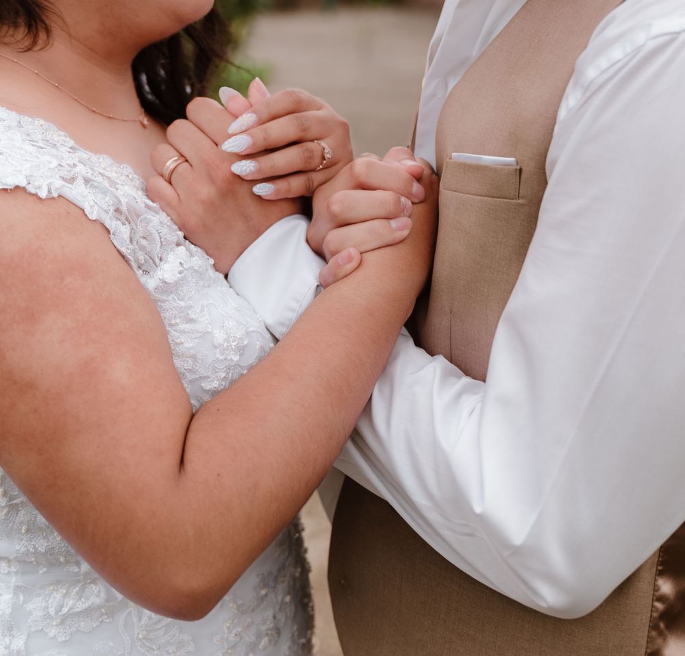 Bride and groom holding hands at wedding ceremony, bride wearing lace dress with manicured nails and wedding ring.