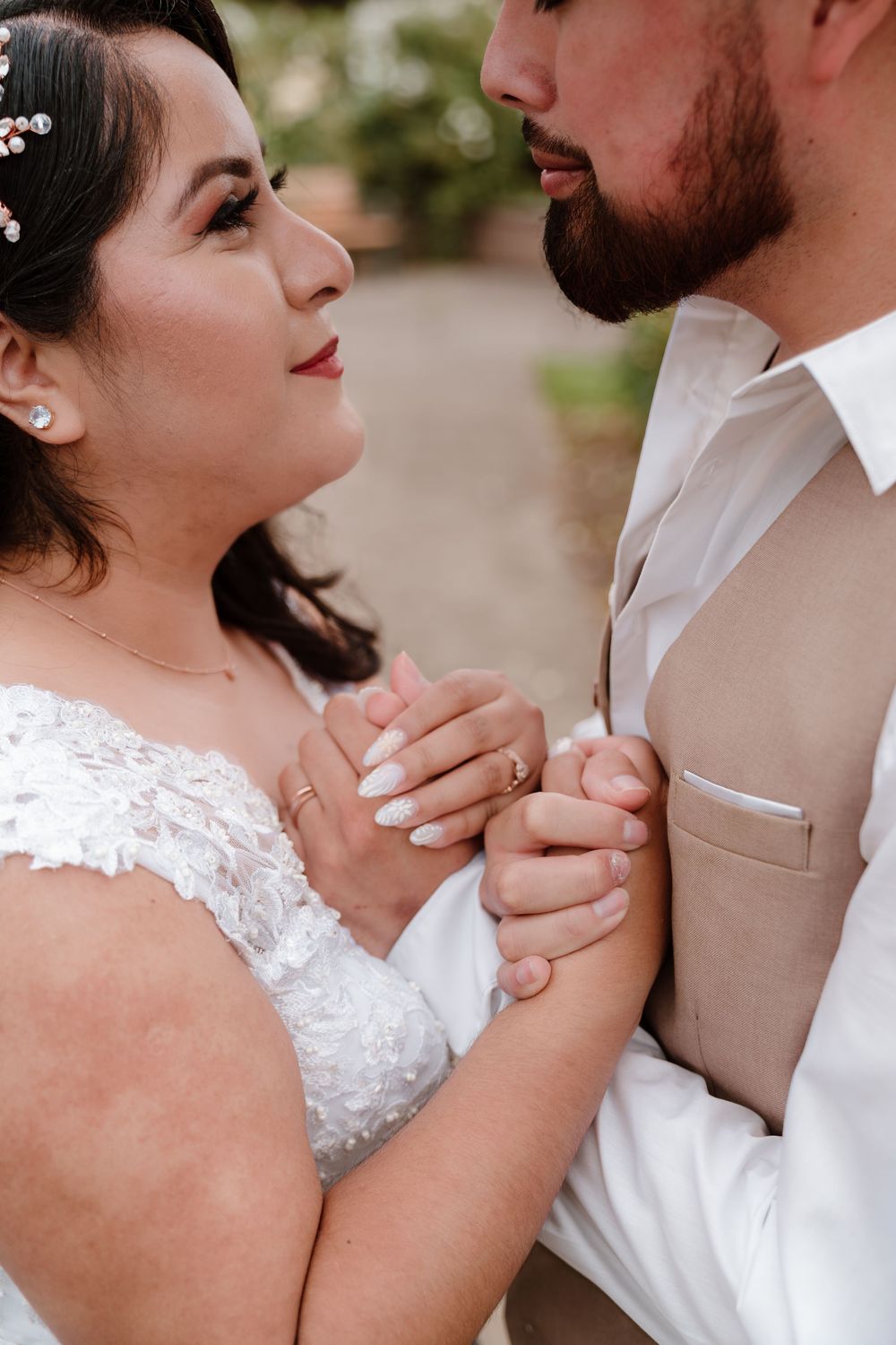 A bride and groom share a tender moment, holding hands closely as she gazes up at him in wedding attire.