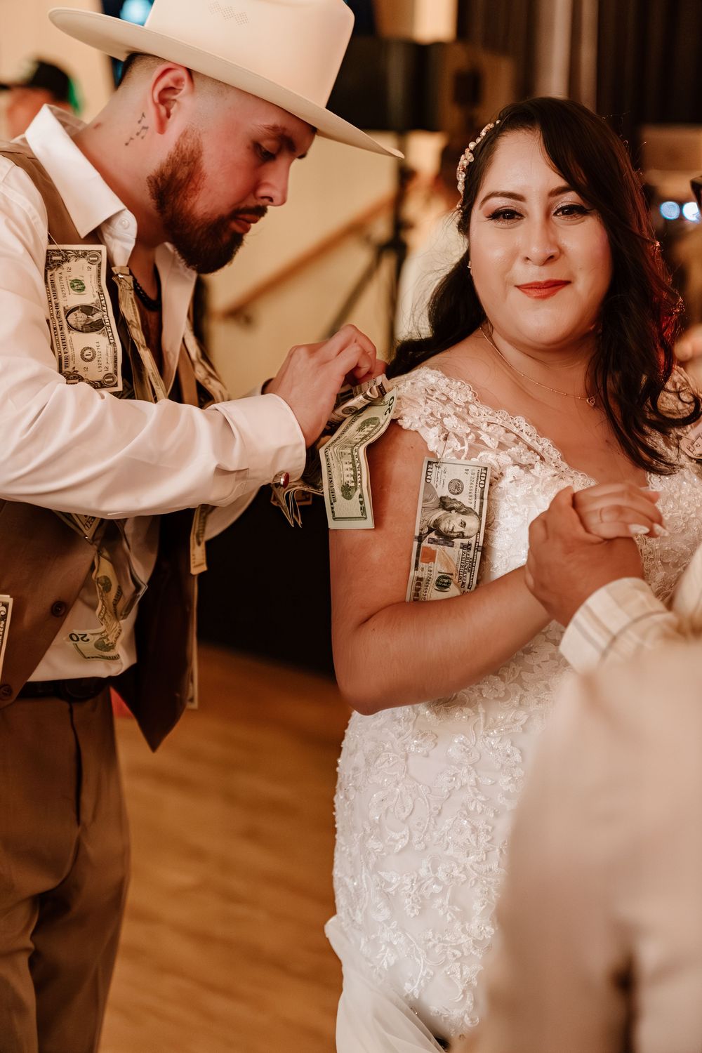 Bride and groom sharing a dollar dance at rustic wedding reception, groom wearing cowboy hat pinning money to bride's dress.