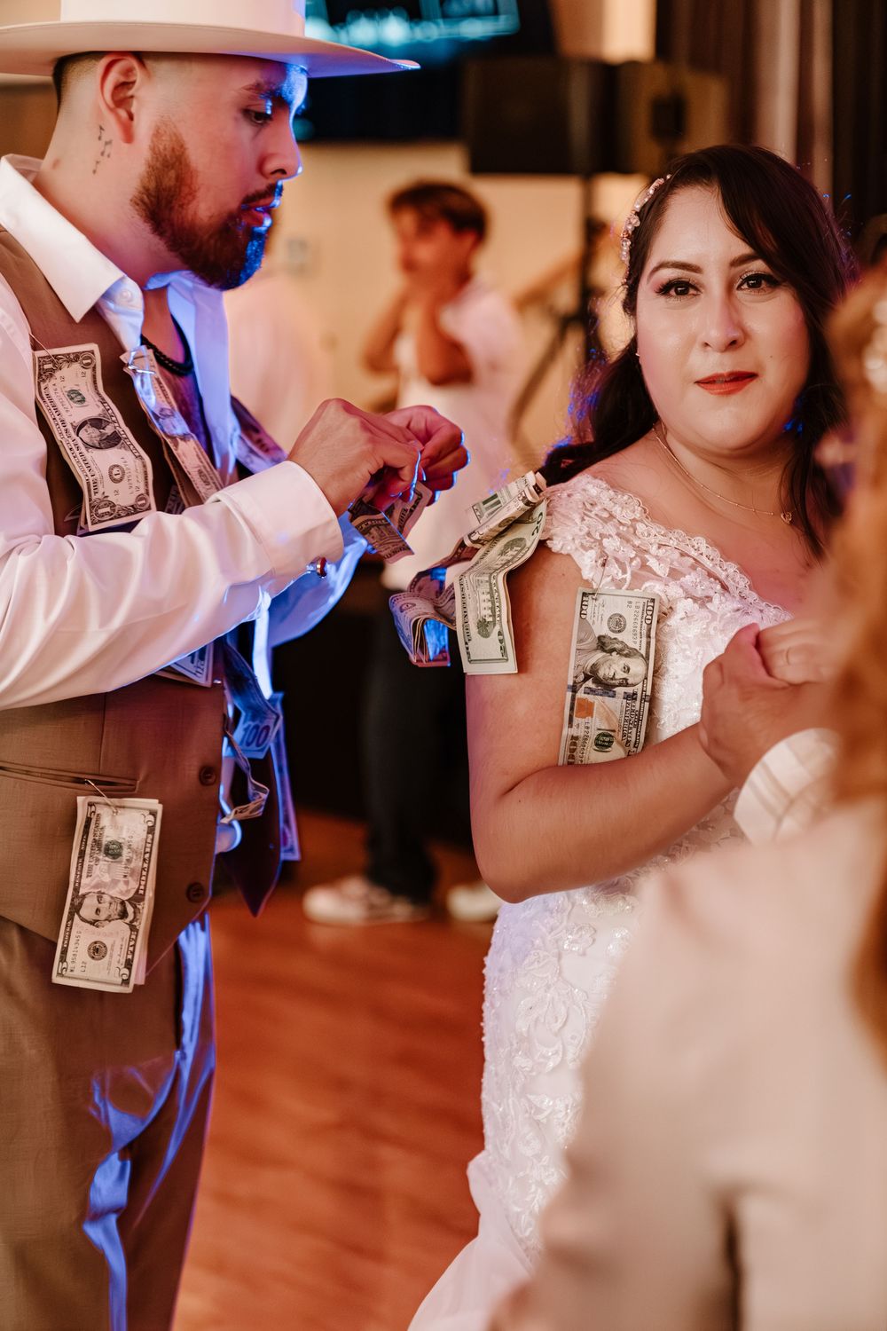 Bride and groom pinning dollar bills on wedding attire during traditional money dance celebration at reception.