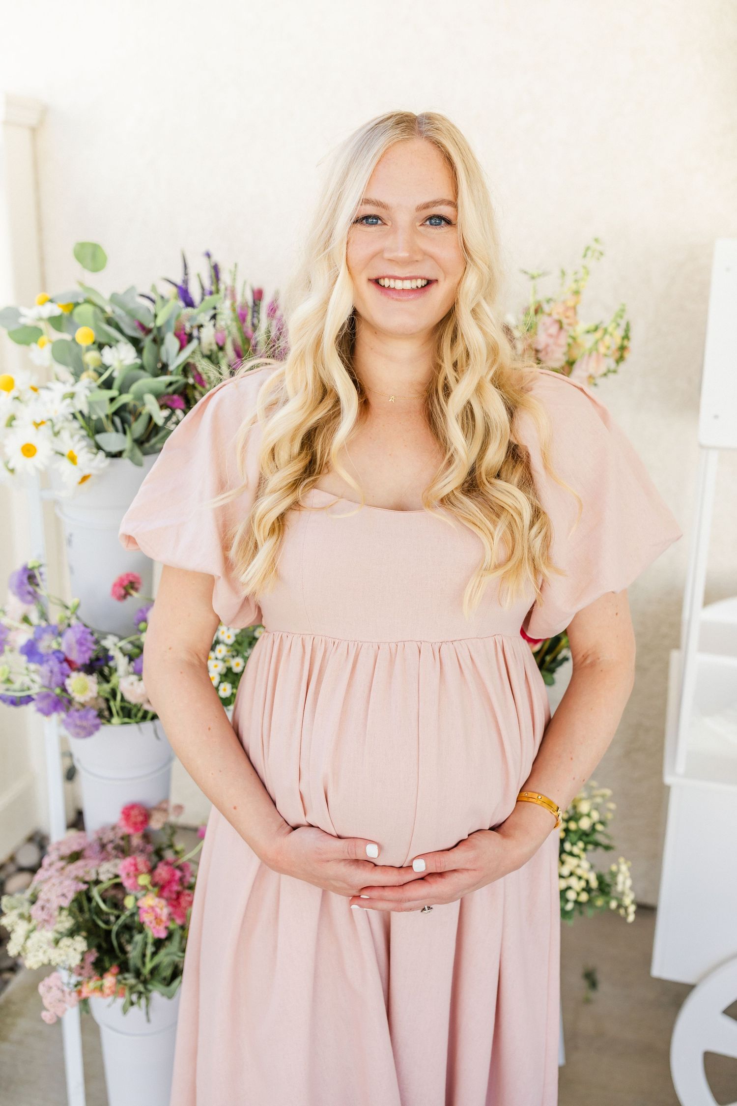 Portrait of Woman in light pink ruffle dress poses in front of floral backdrop in bright white room by Chelsee Rawe Photography
