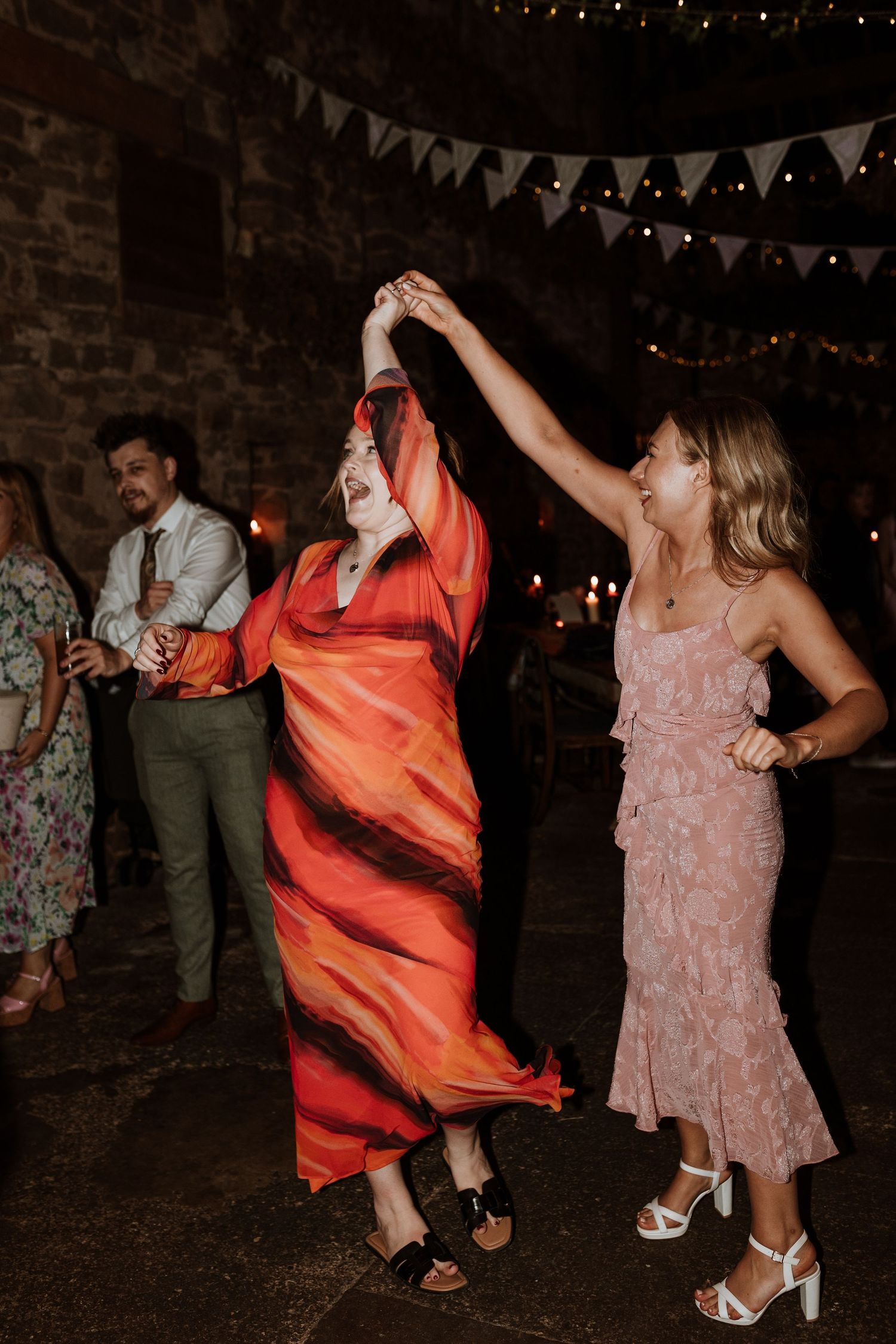 Wedding guests dance energetically on a dark dance floor under twinkling lights and bunting decorations.