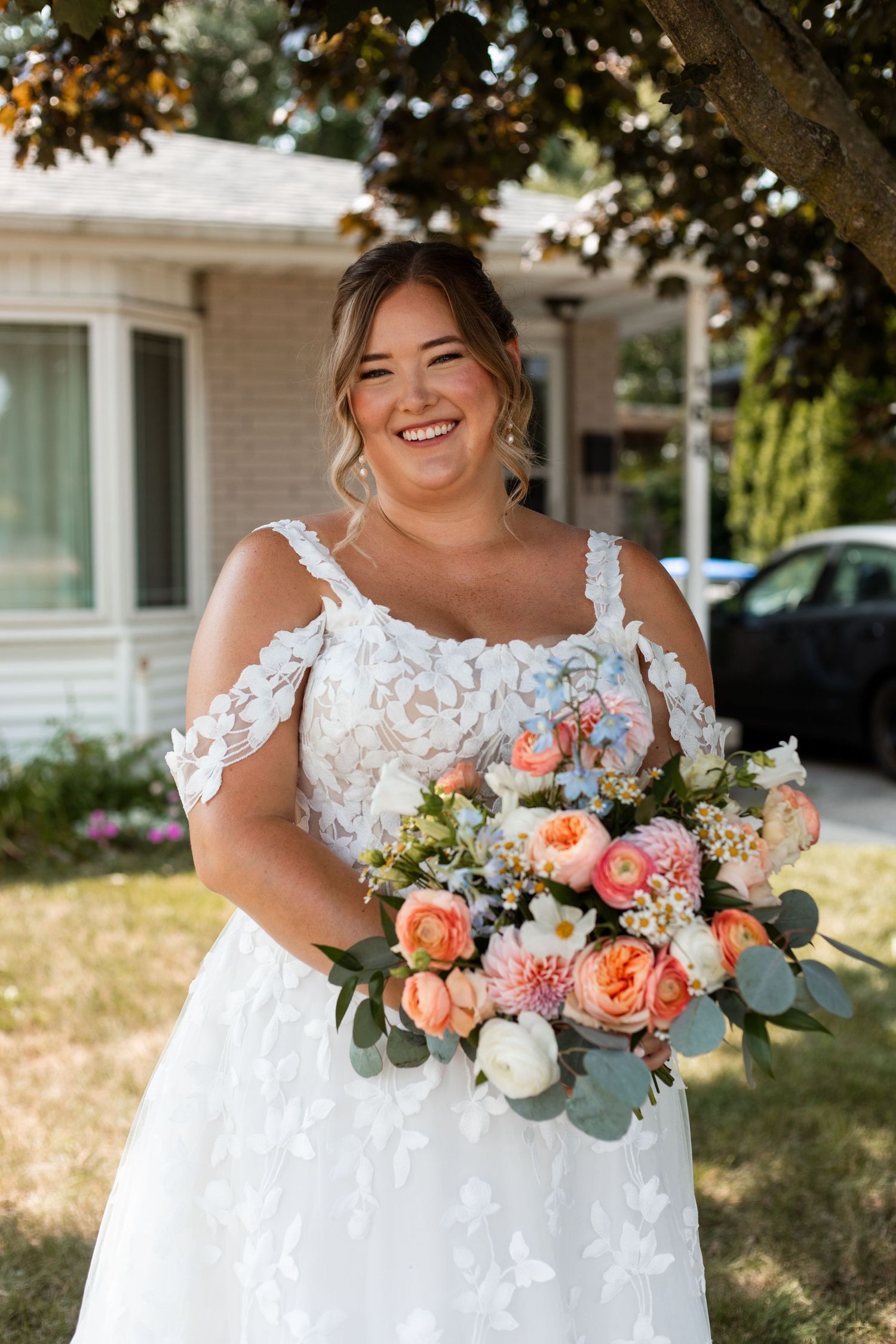 A beautiful bridal bouquet featuring coral roses, white flowers and eucalyptus leaves against a white lace dress.