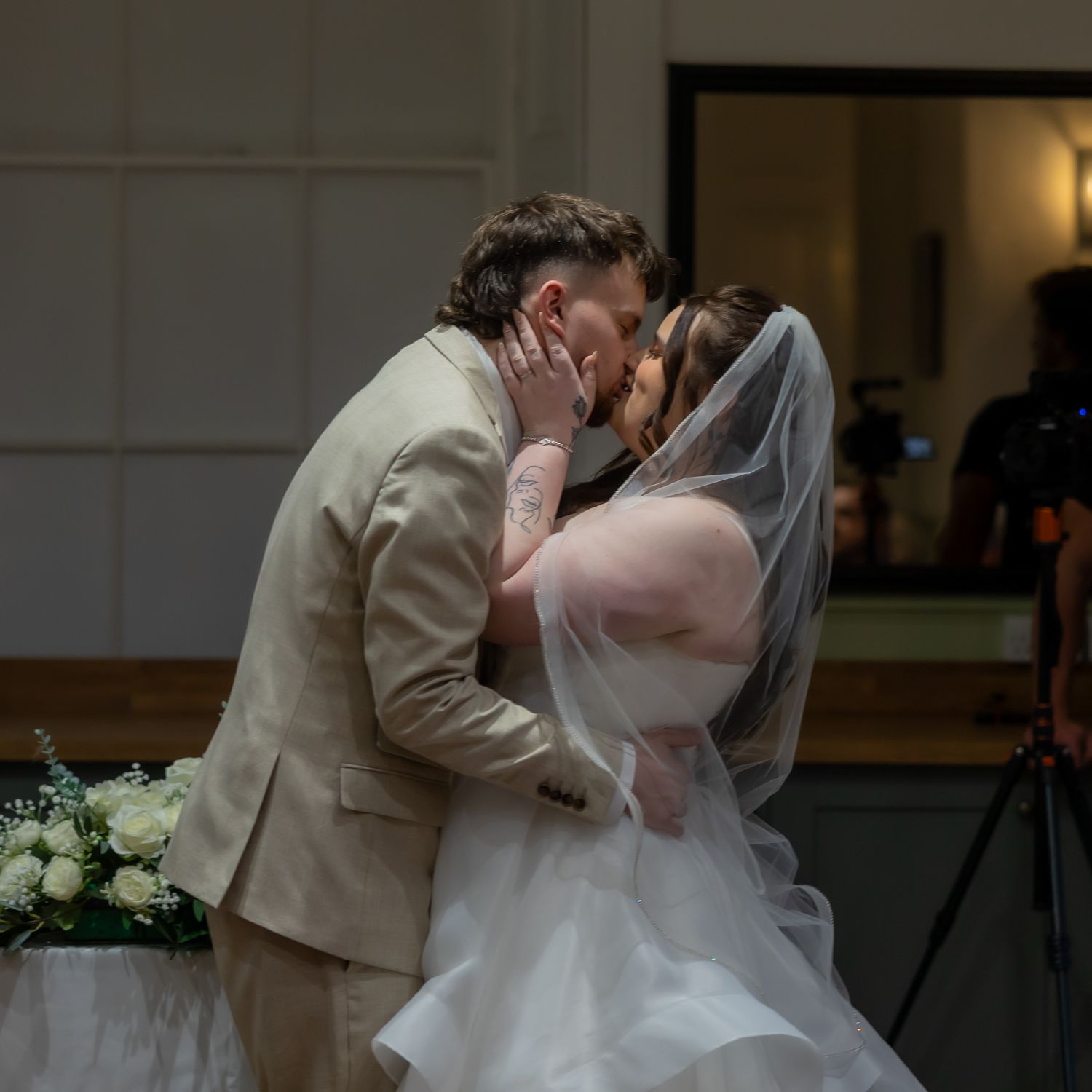 A couple in formal wedding attire shares a romantic dip during their wedding at an elegant indoor venue.