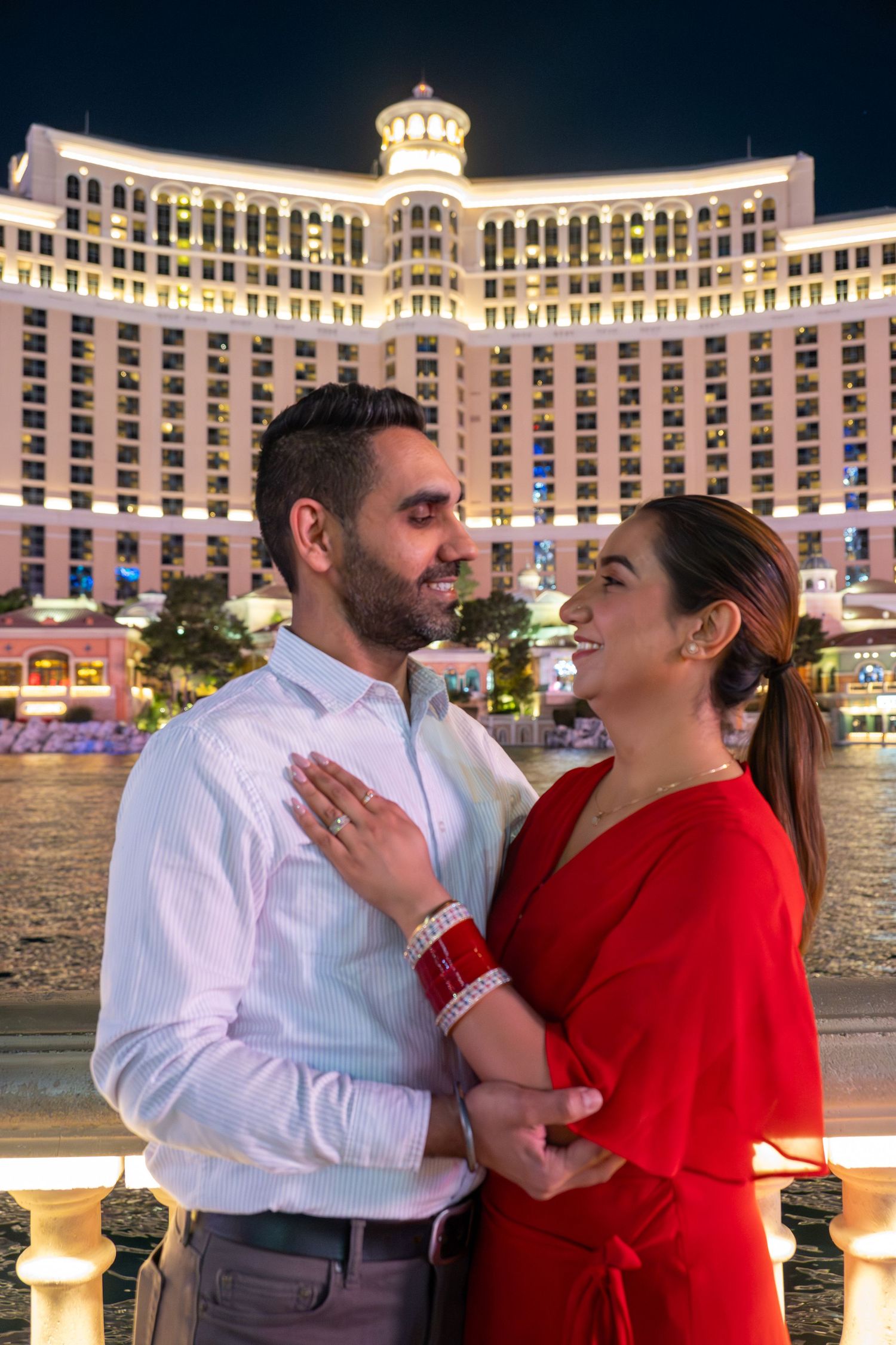 Happy couple embracing and laughing in front of the lit-up Bellagio Hotel in Las Vegas at night.
