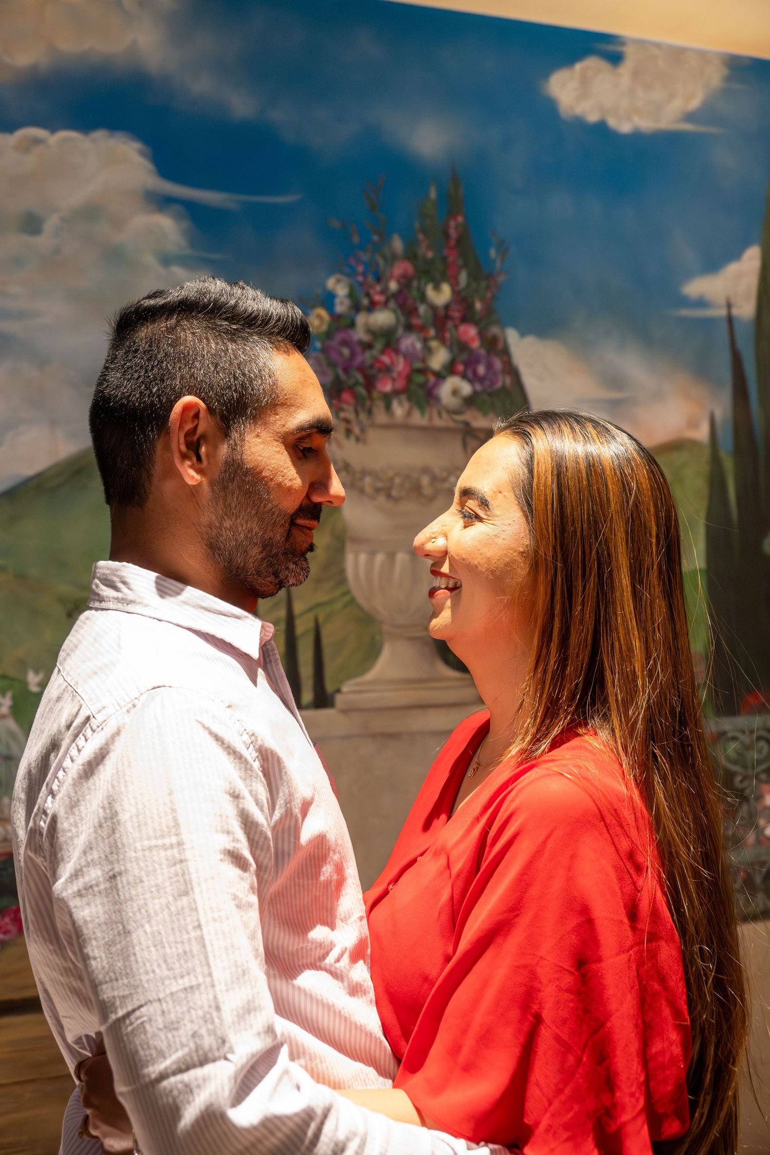 Happy couple gazing lovingly at each other in front of a vibrant painted landscape backdrop.