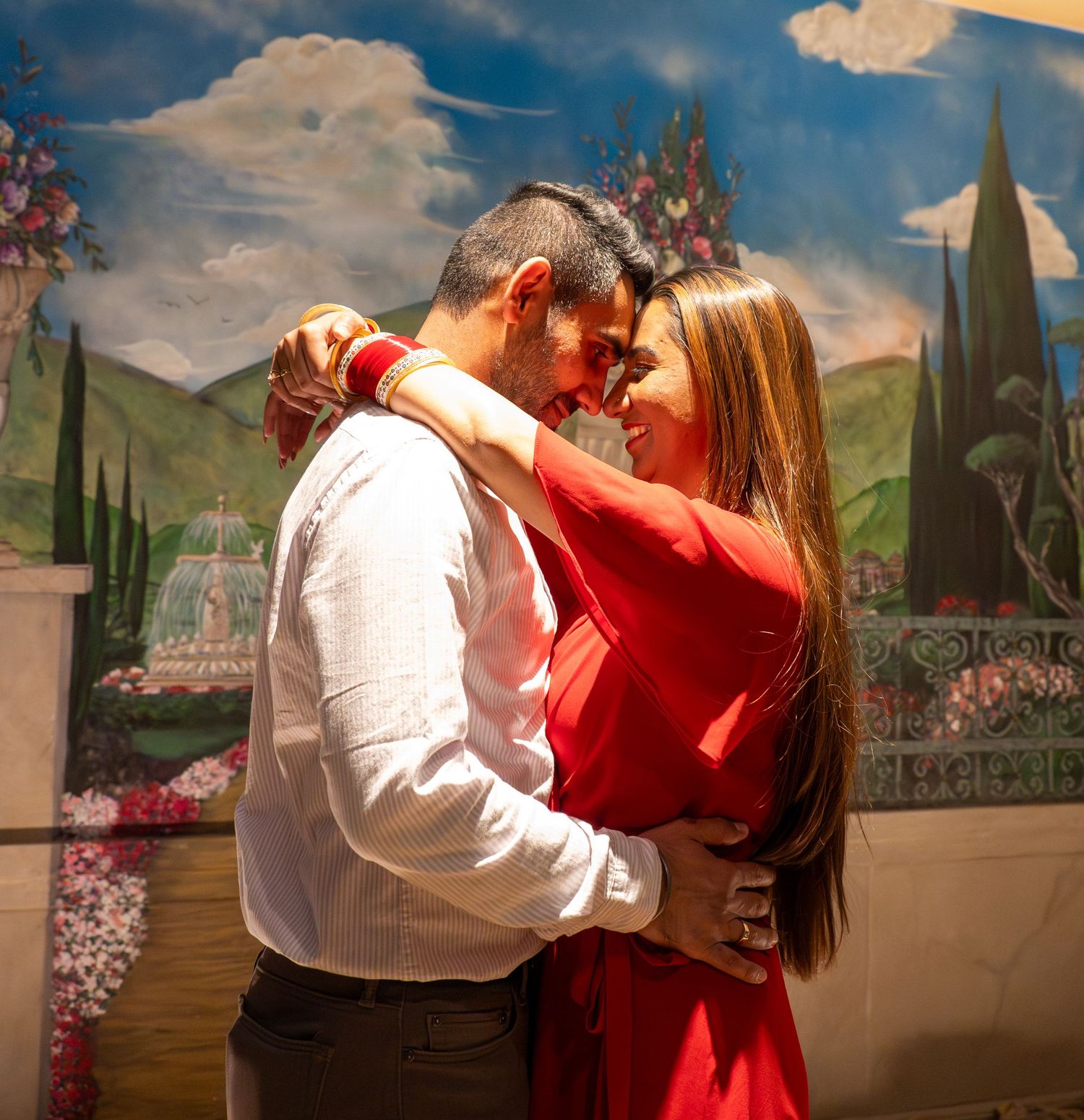 Romantic couple embracing and smiling at each other in front of a colorful garden mural painting.