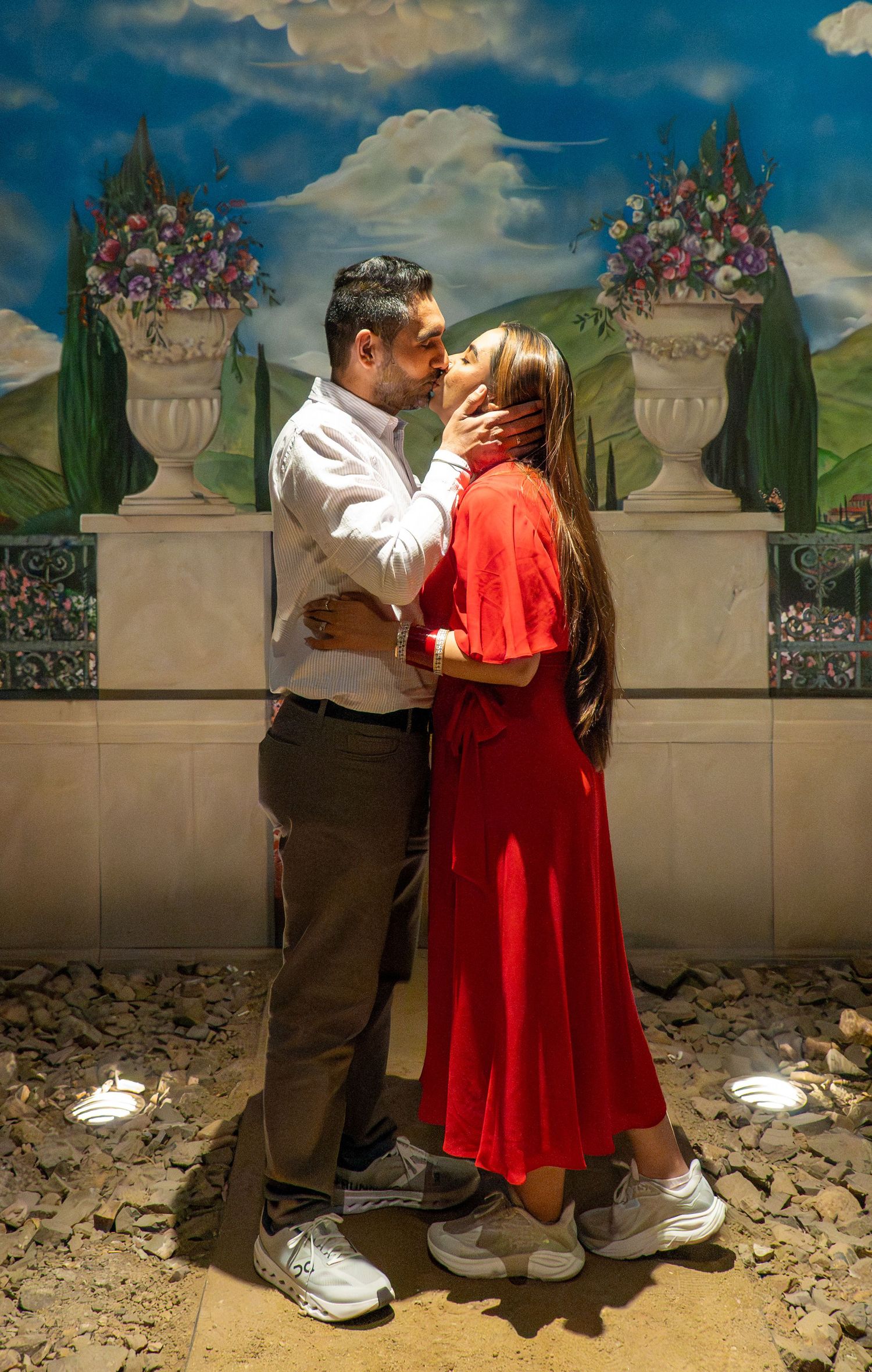 Couple kissing passionately in front of an ornate Italian garden mural with cypress trees.