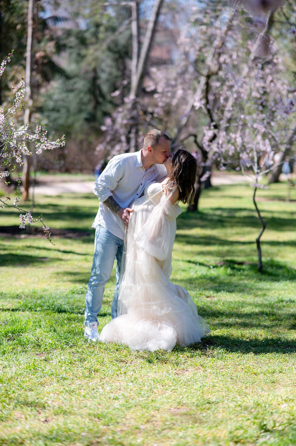 A couple dances together under blooming cherry blossom trees in a spring garden setting.