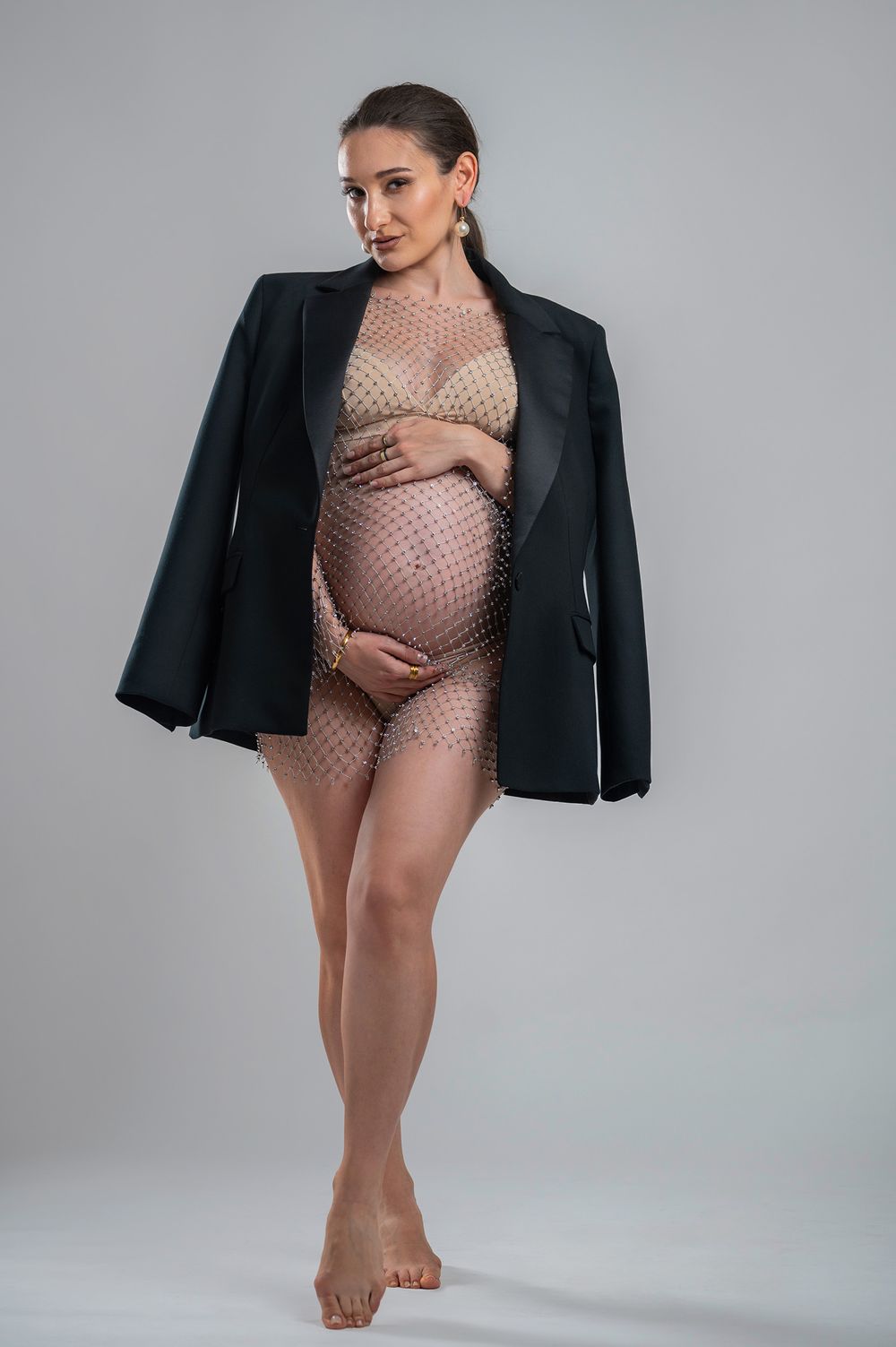 Fashion photo series of a model in a beige bodysuit and black blazer striking different poses against a grey backdrop.
