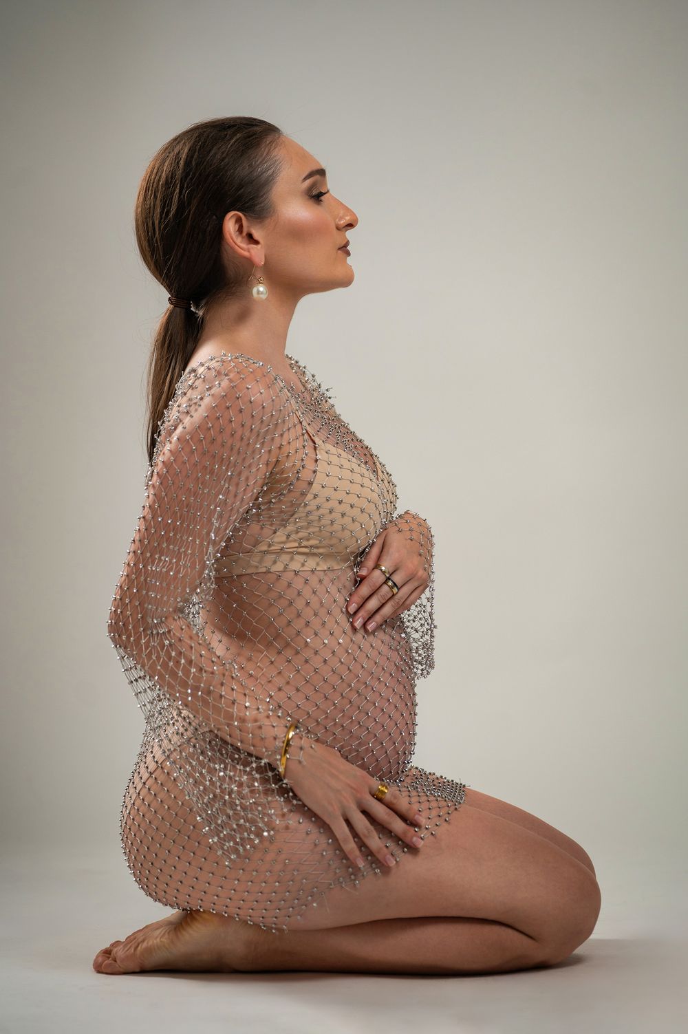 A series of artistic nude photographs showing a figure draped in translucent beaded mesh fabric against a neutral background.