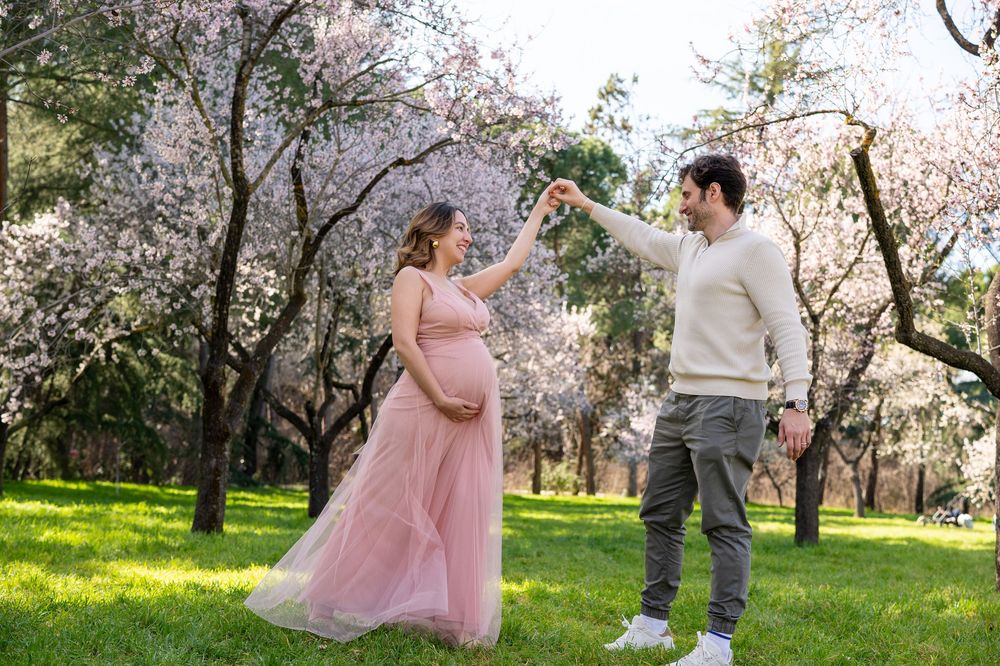 A couple dances together in a blooming spring garden with cherry blossoms, wearing pink dress and casual attire.