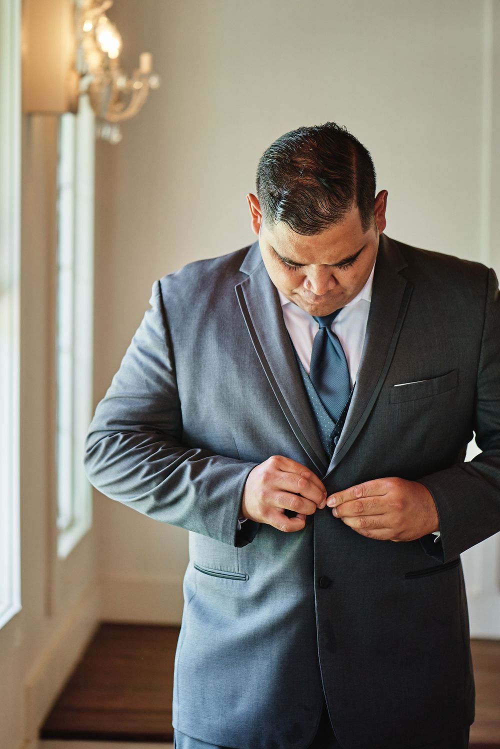 Someone adjusts the buttons on their formal gray suit jacket in a sunlit room.