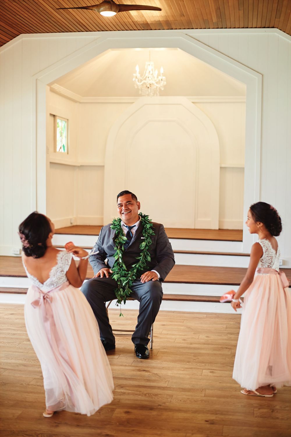 Wedding party members dance and play with children in formal attire in a bright reception hall.