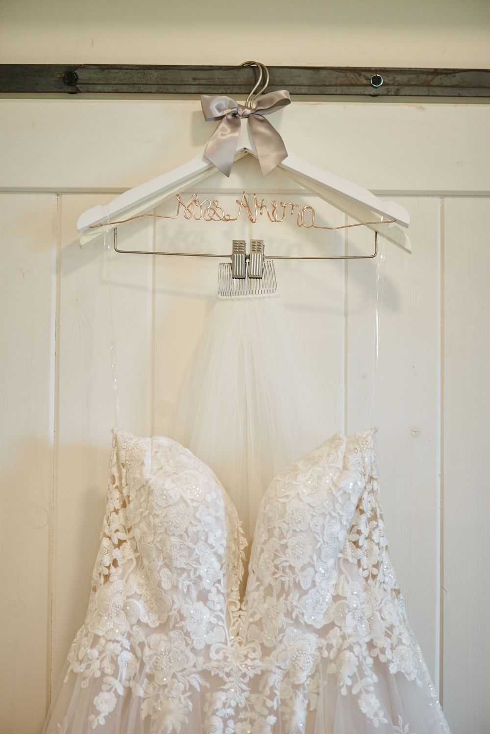 Delicate white lace wedding dress hanging on display against white paneled walls.