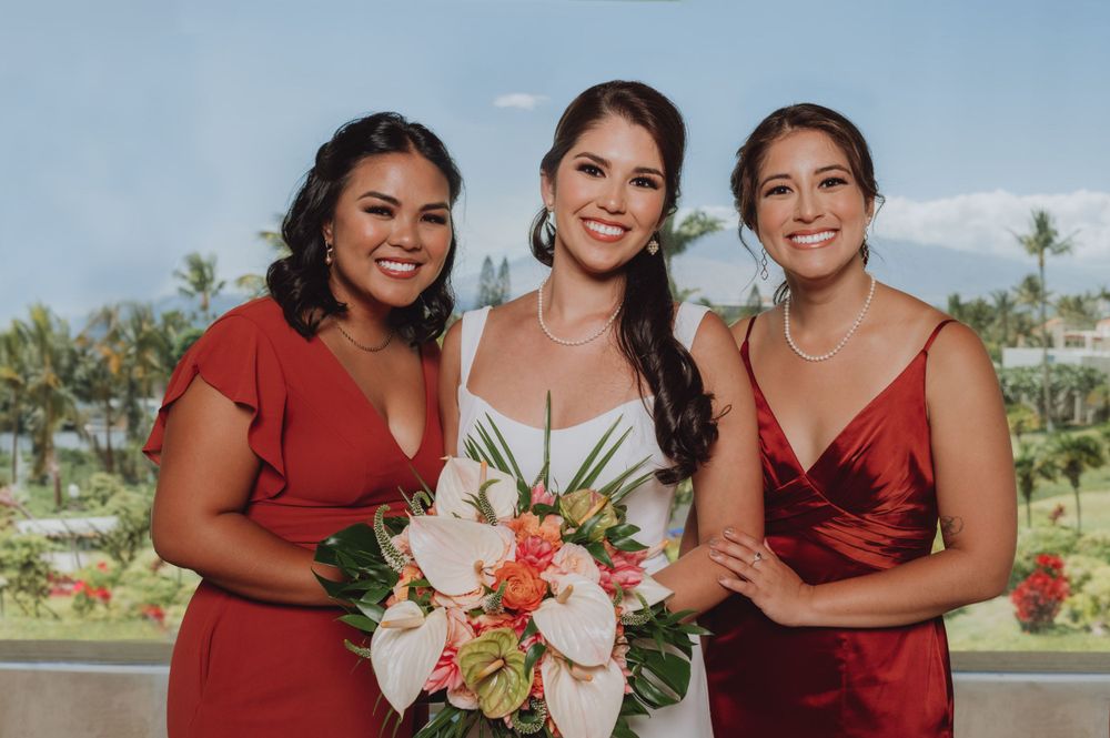 Wedding party members in burgundy dresses smiling against blue sky backdrop.