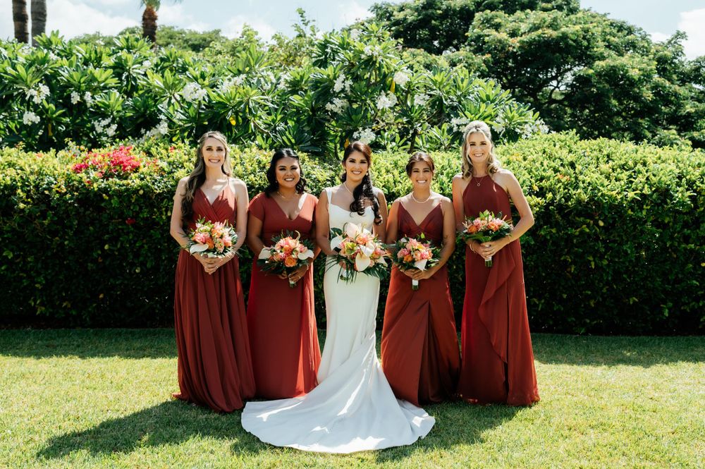 Wedding party in burgundy dresses and white gown arranged on grassy lawn.