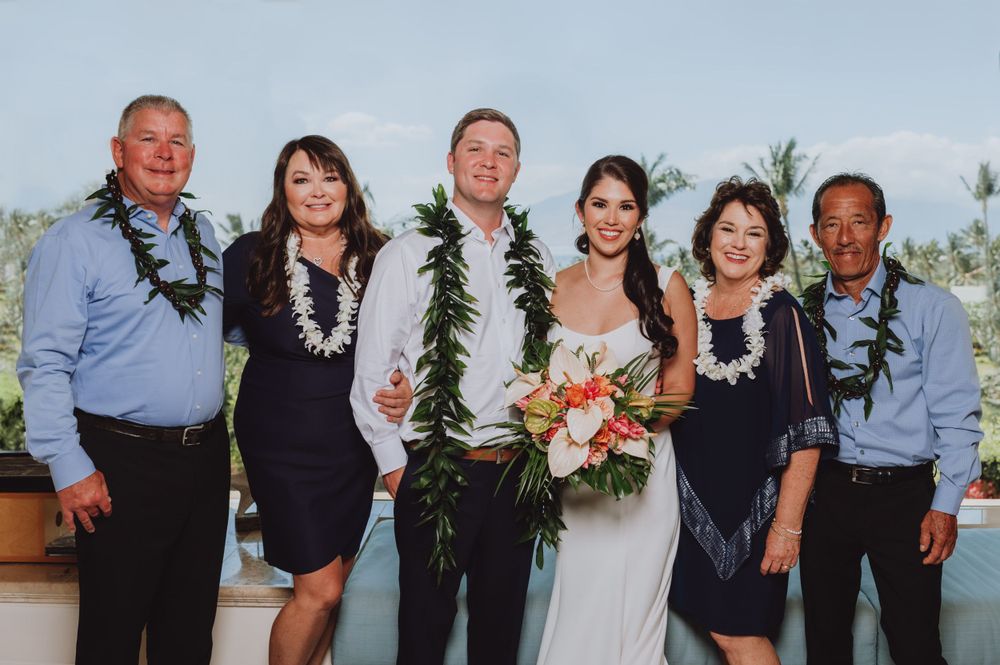 Wedding celebration group photo with guests in casual attire against ocean backdrop.