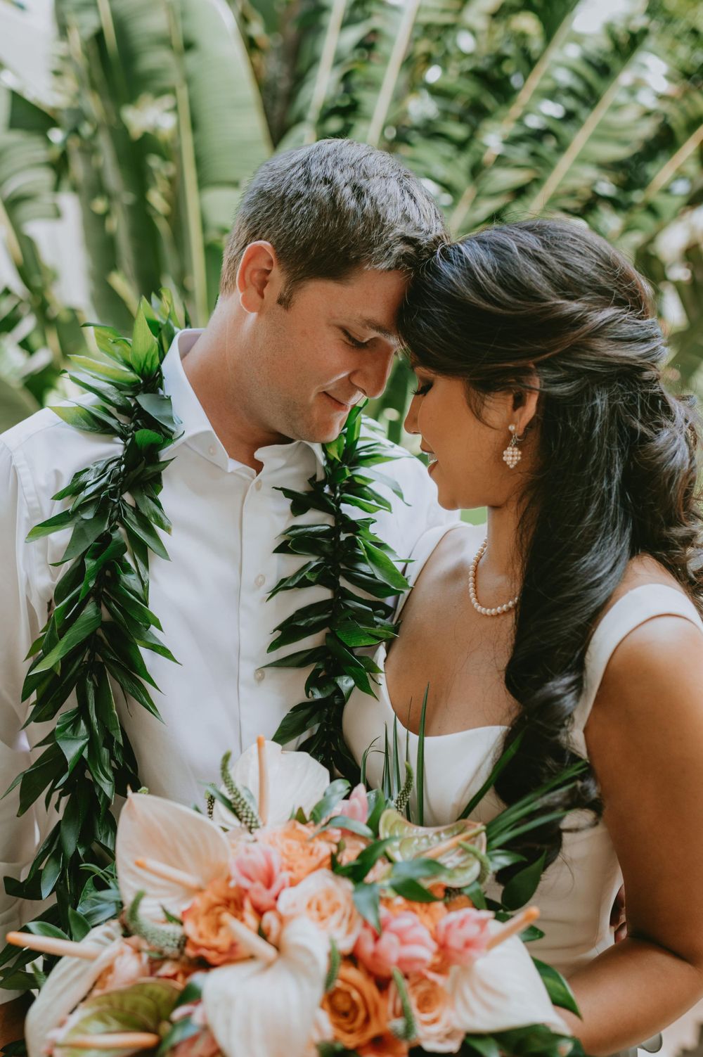 Romantic wedding moment with traditional Hawaiian lei garlands and coral bouquet.
