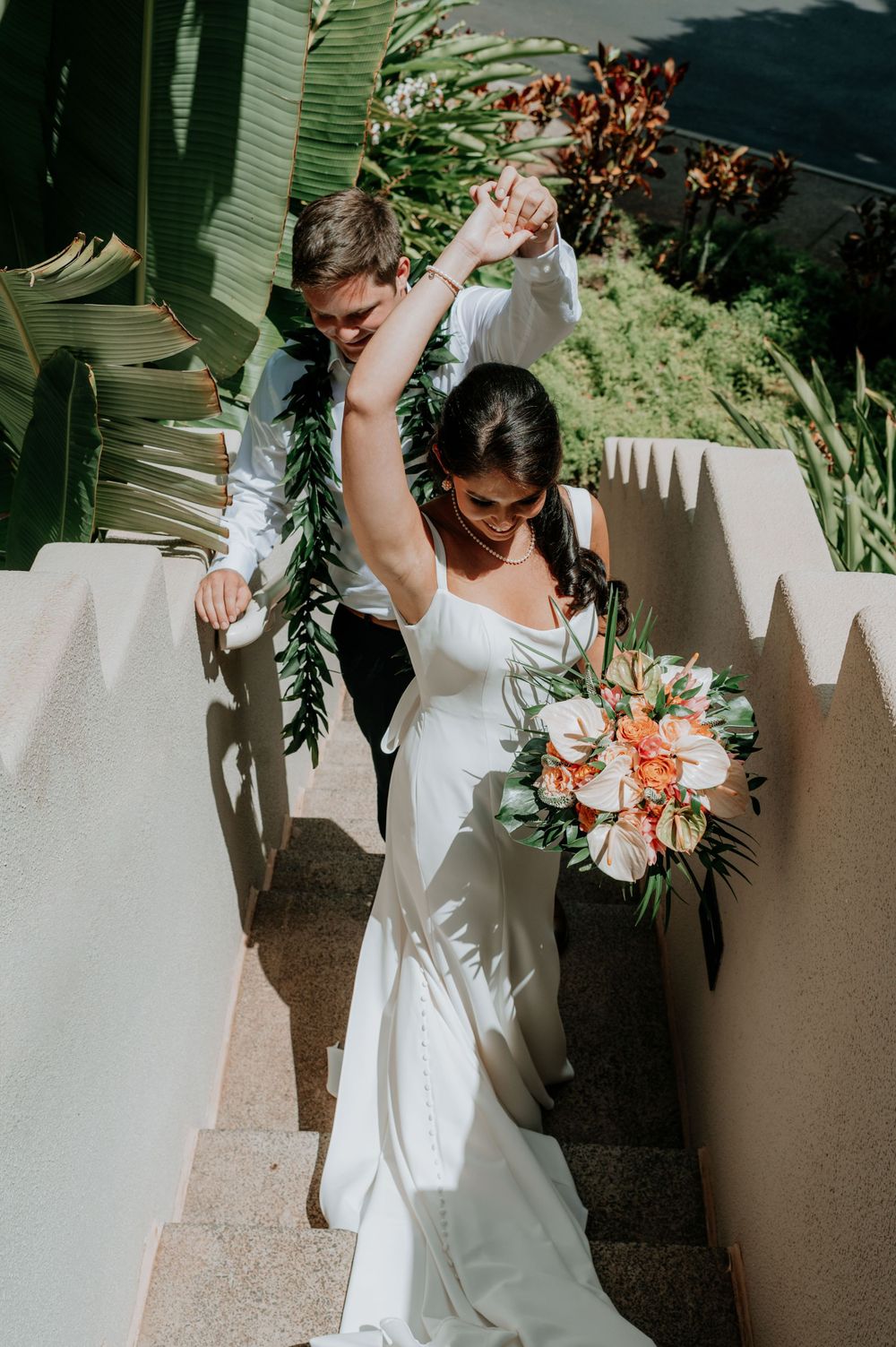 Beautiful wedding bouquet with coral and peach flowers against a white wall with tropical greenery.