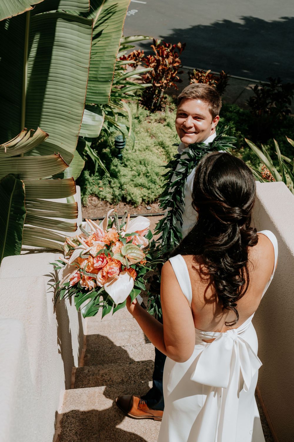 Wedding couple posing with tropical foliage and floral arrangements outdoors.