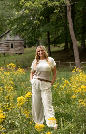 Outdoor portrait session in a field of yellow flowers with rustic wooden fencing and trees in the background.