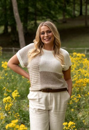 Woman in cream knit top and linen pants poses in a garden with blooming yellow wildflowers on a sunny day.